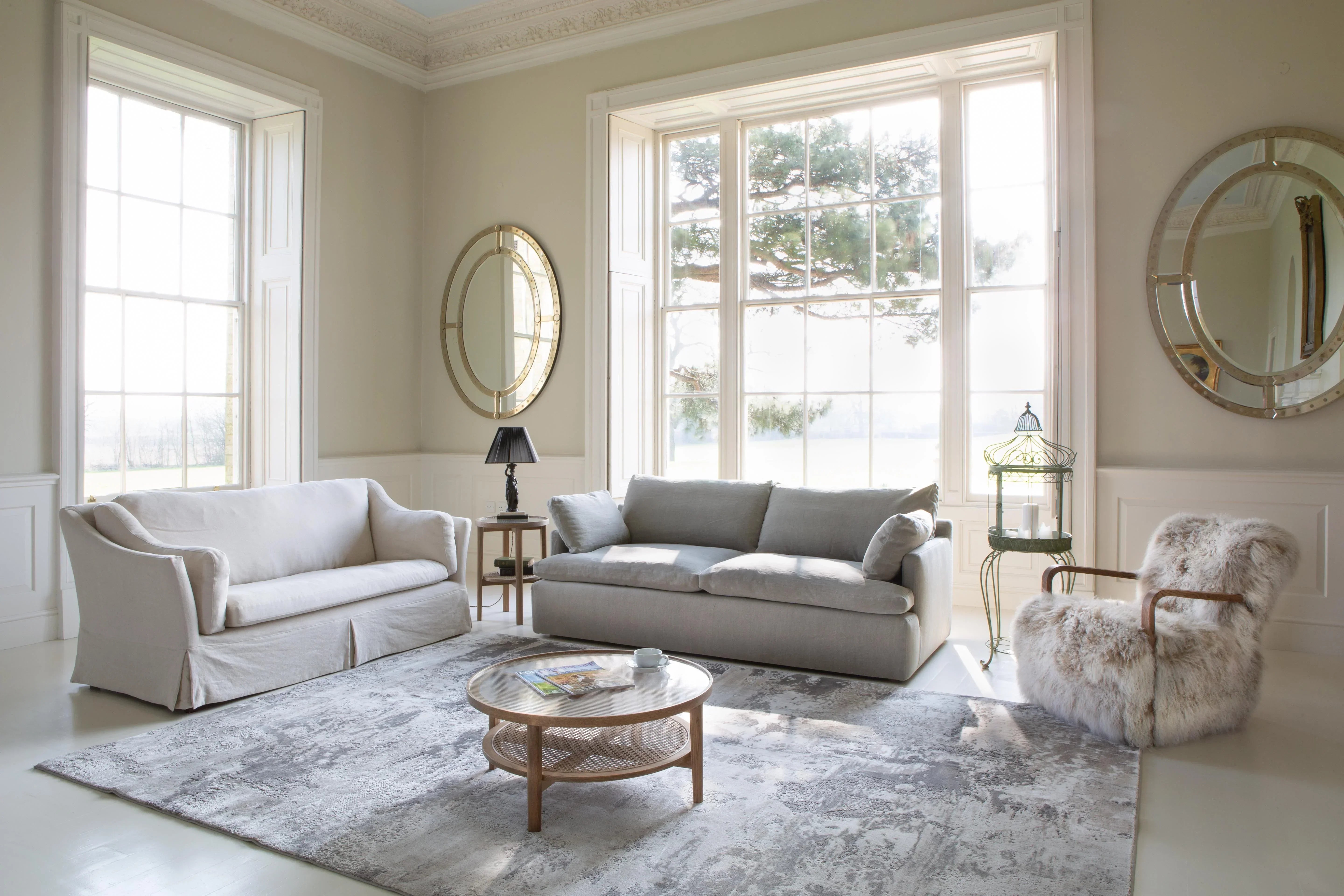 Light grey sofas and faux fur armchair in bright living room with large windows and mirrors