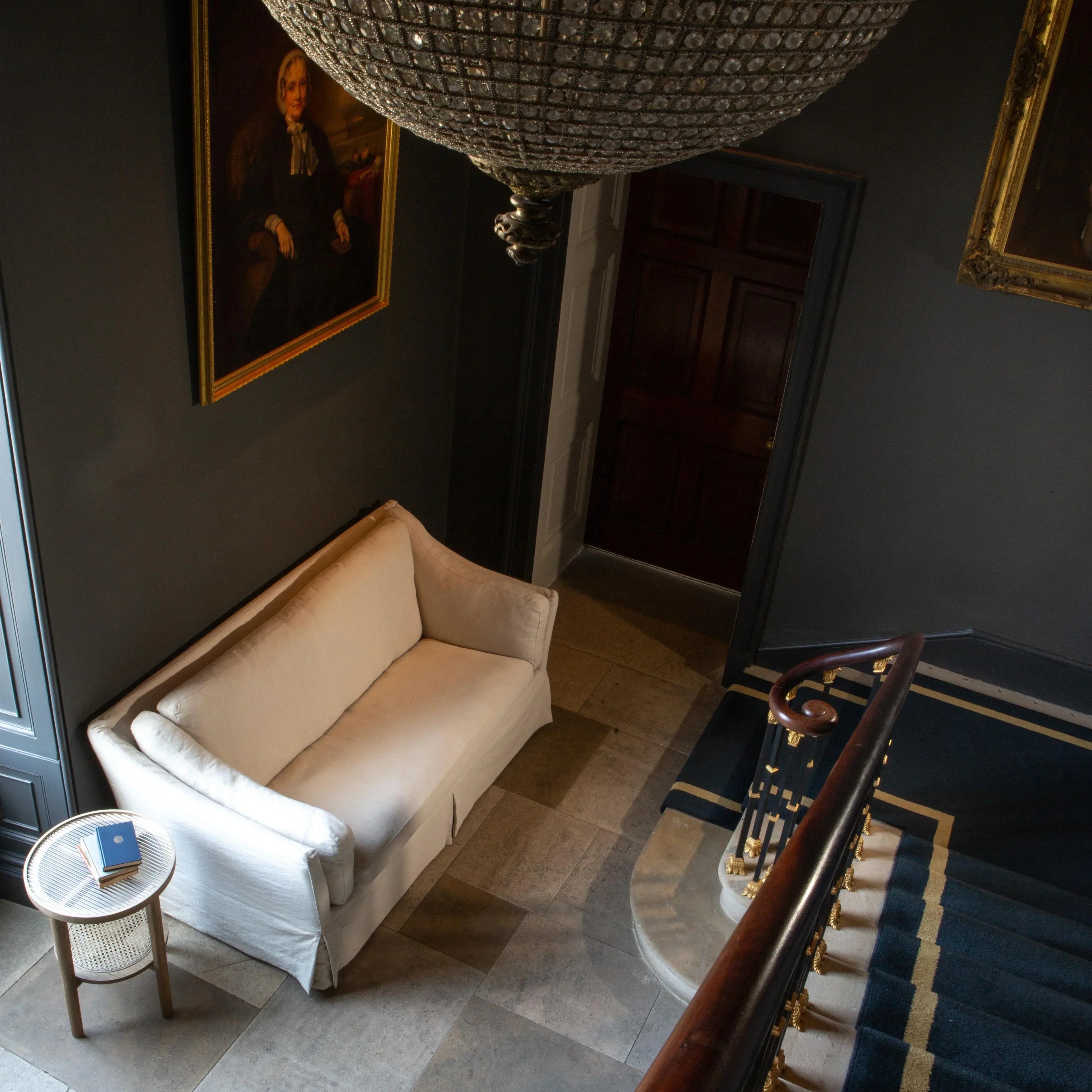 White fabric sofa beside round side table in hallway with stone floor and portrait on wall