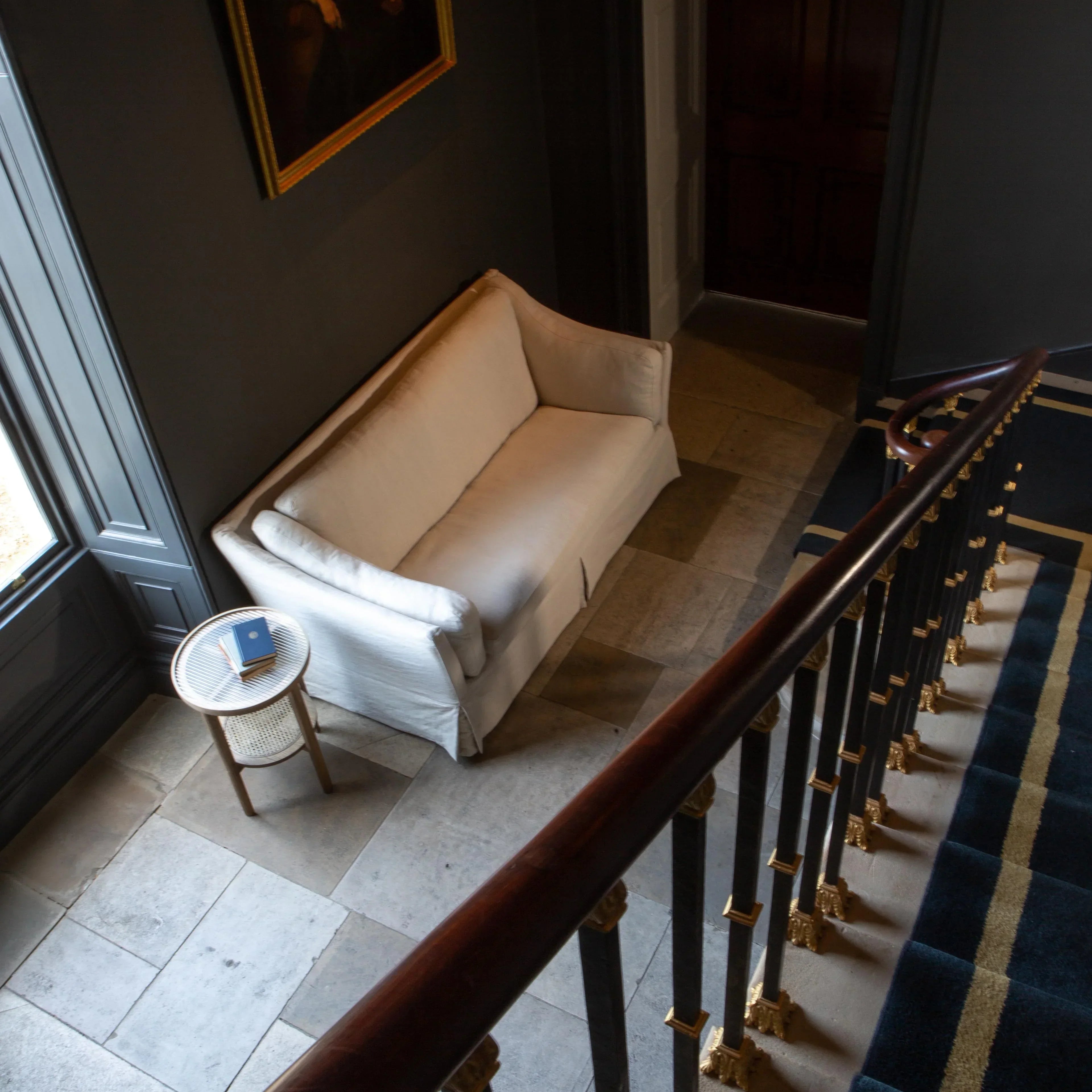 Cream fabric sofa with side table in hallway next to staircase and dark wall décor