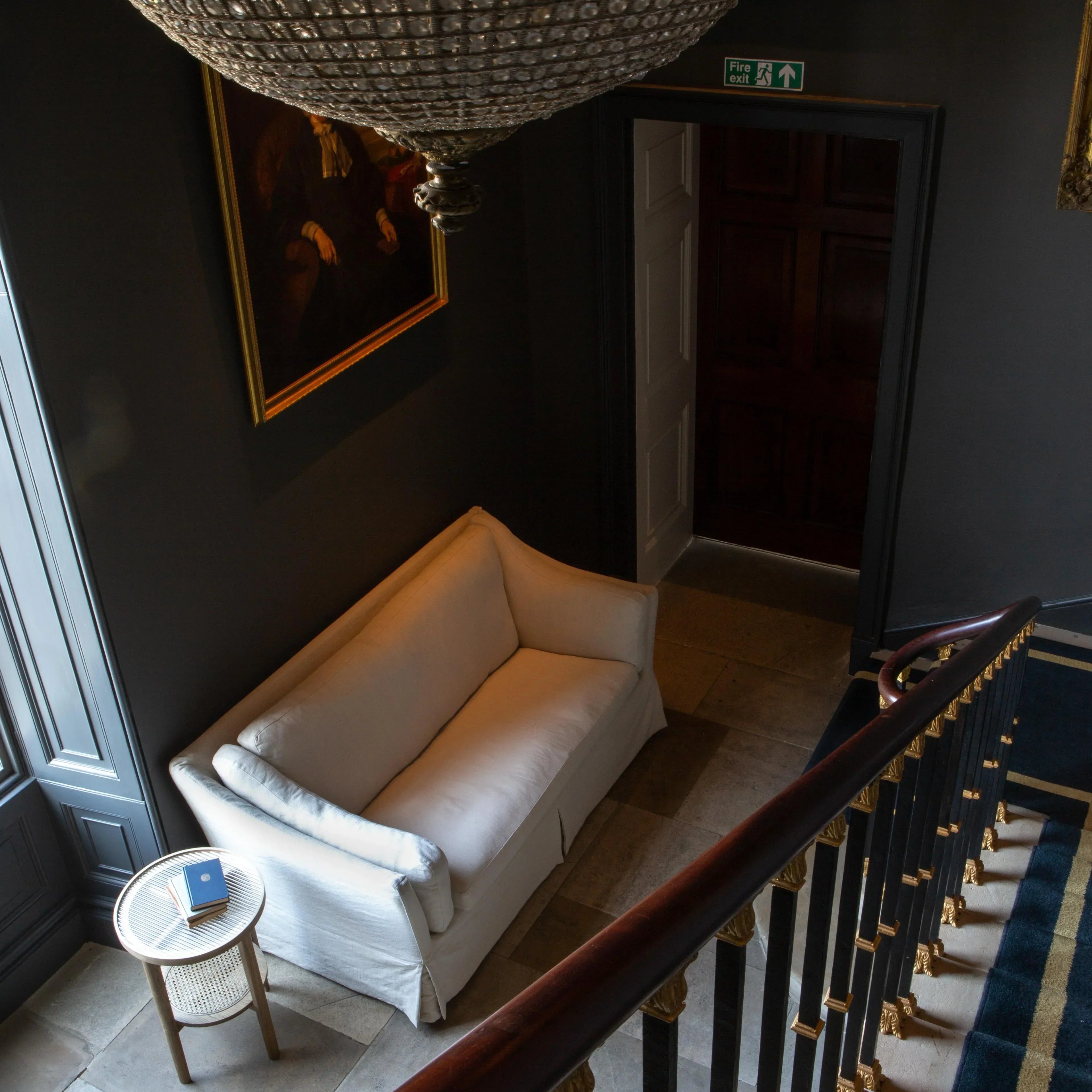 Cream fabric sofa in hallway beside round wooden side table and staircase with gold accents