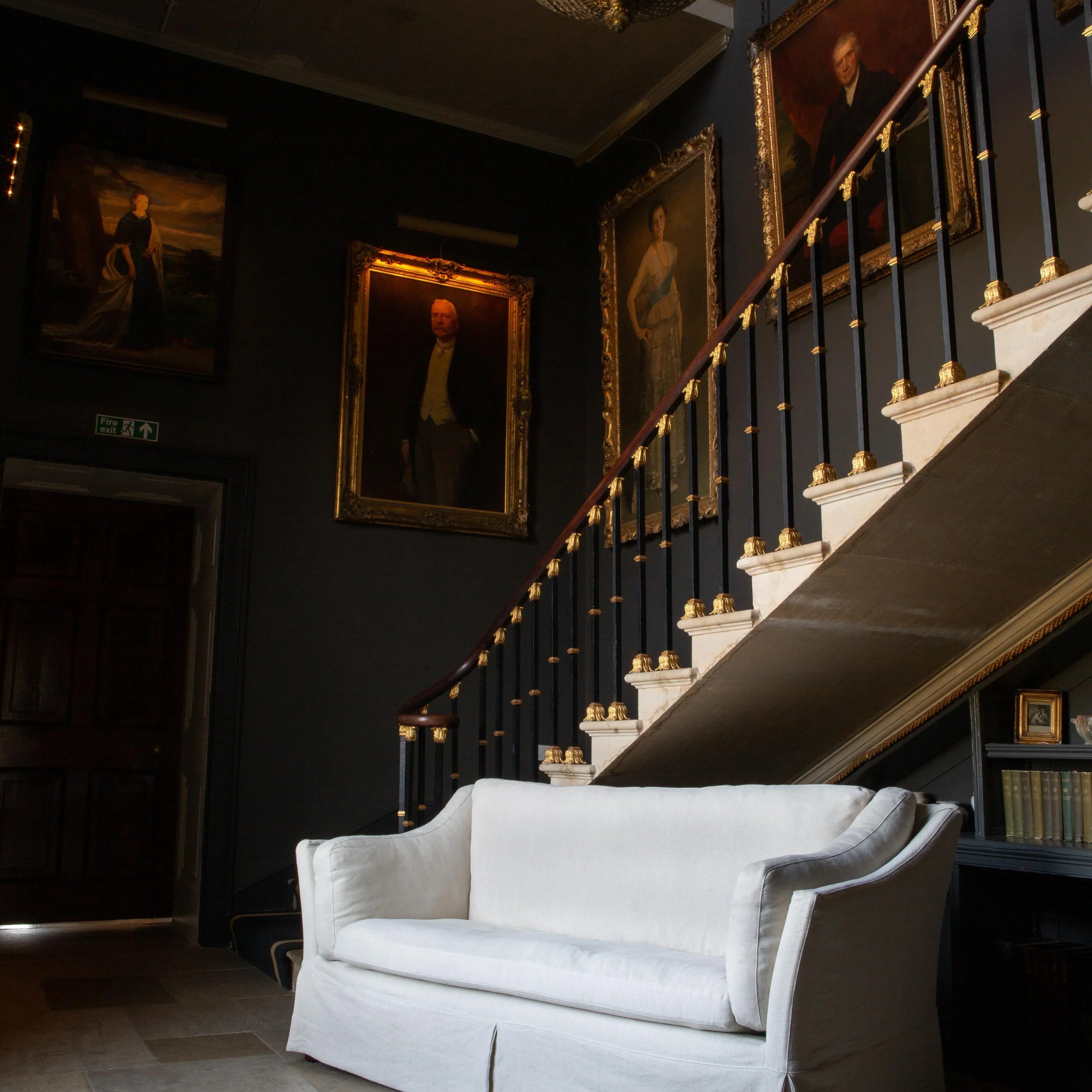 White fabric sofa placed in a classic hallway beneath staircase and framed portraits