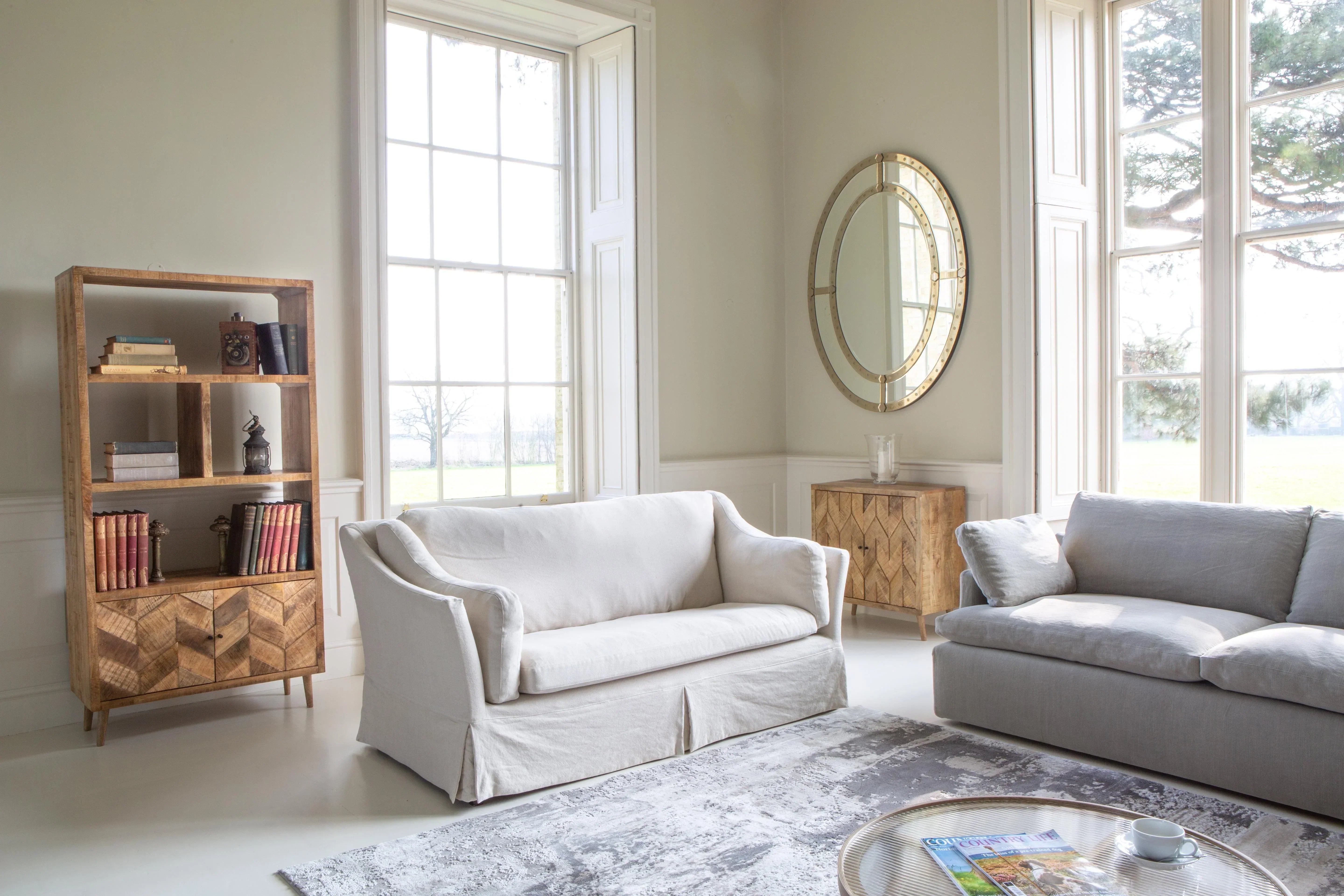 Light grey sofa set in bright living room with large windows and wooden bookshelf