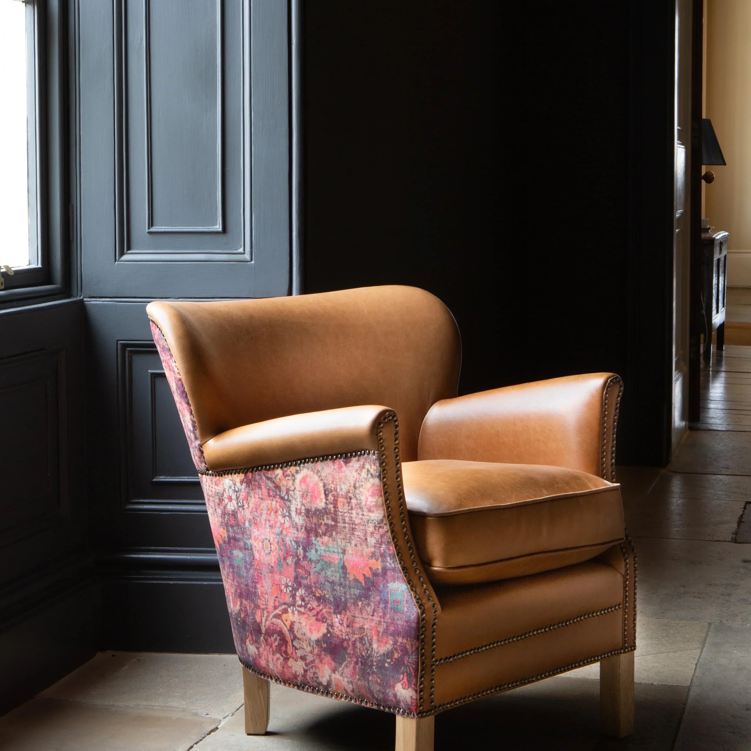 Tan leather armchair with patterned fabric sides and wooden legs in a modern interior