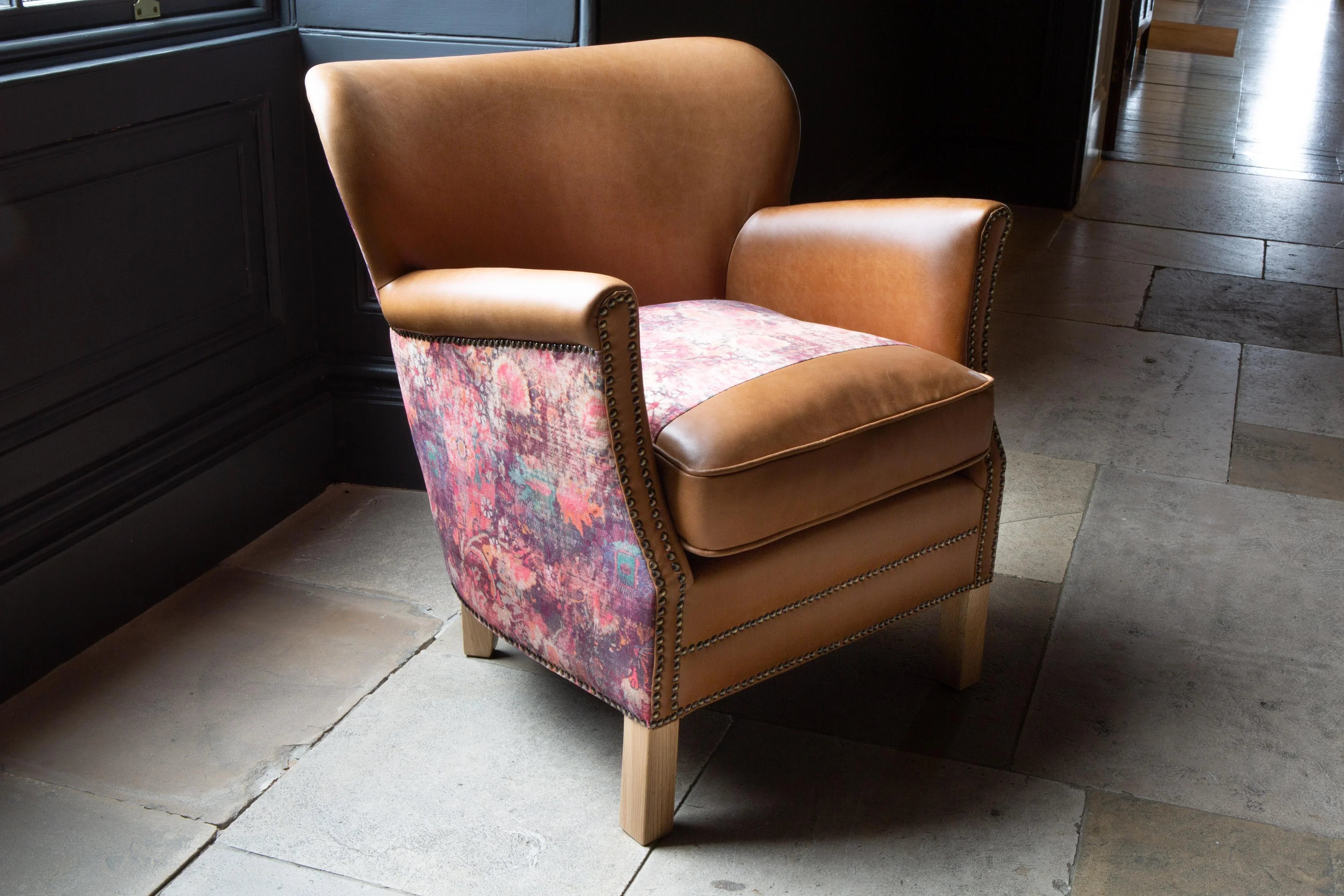 Tan leather accent chair with patterned fabric sides and cushioned seat in natural light