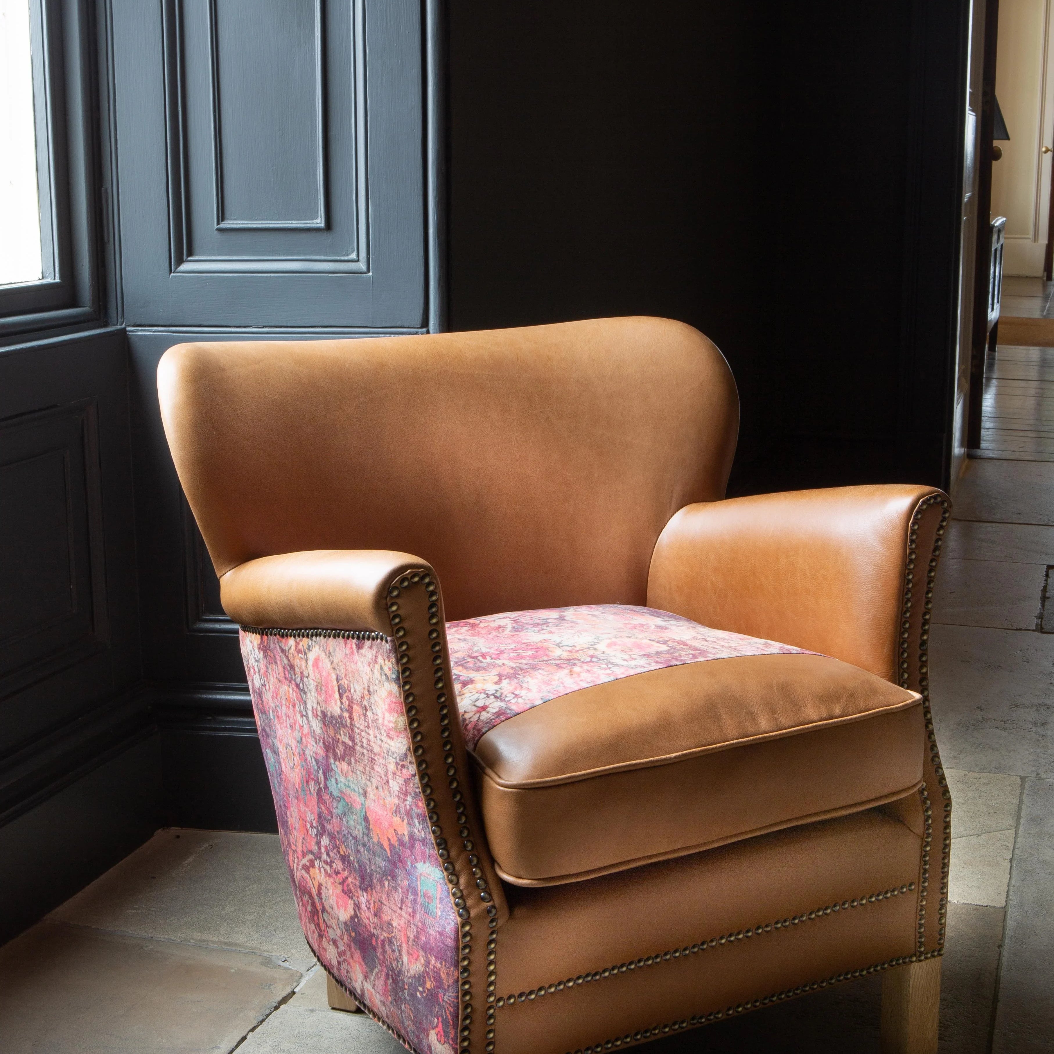 Tan leather armchair with patterned fabric sides and wooden legs near a window