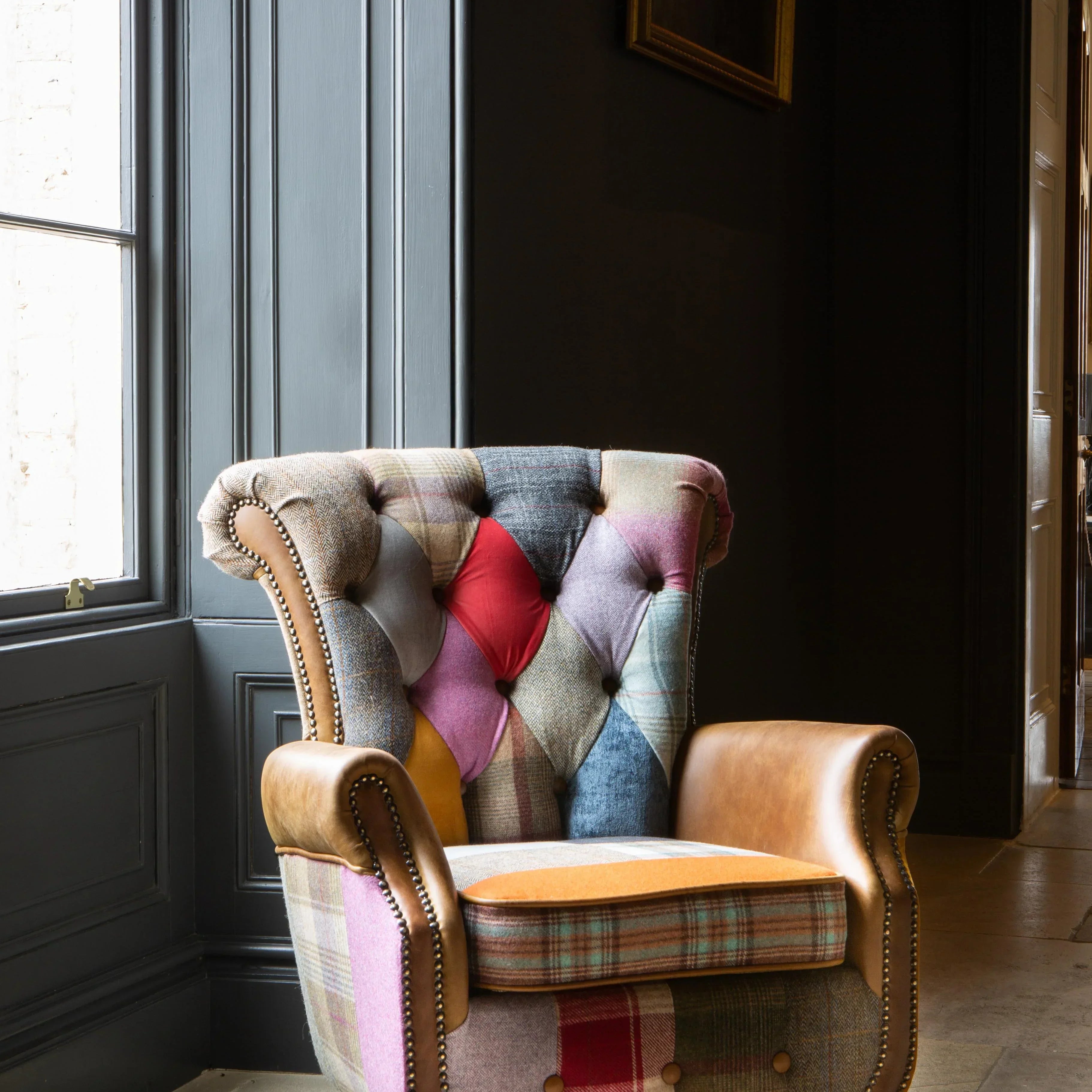 Patchwork armchair with leather arms and wooden legs by a window in a classic interior