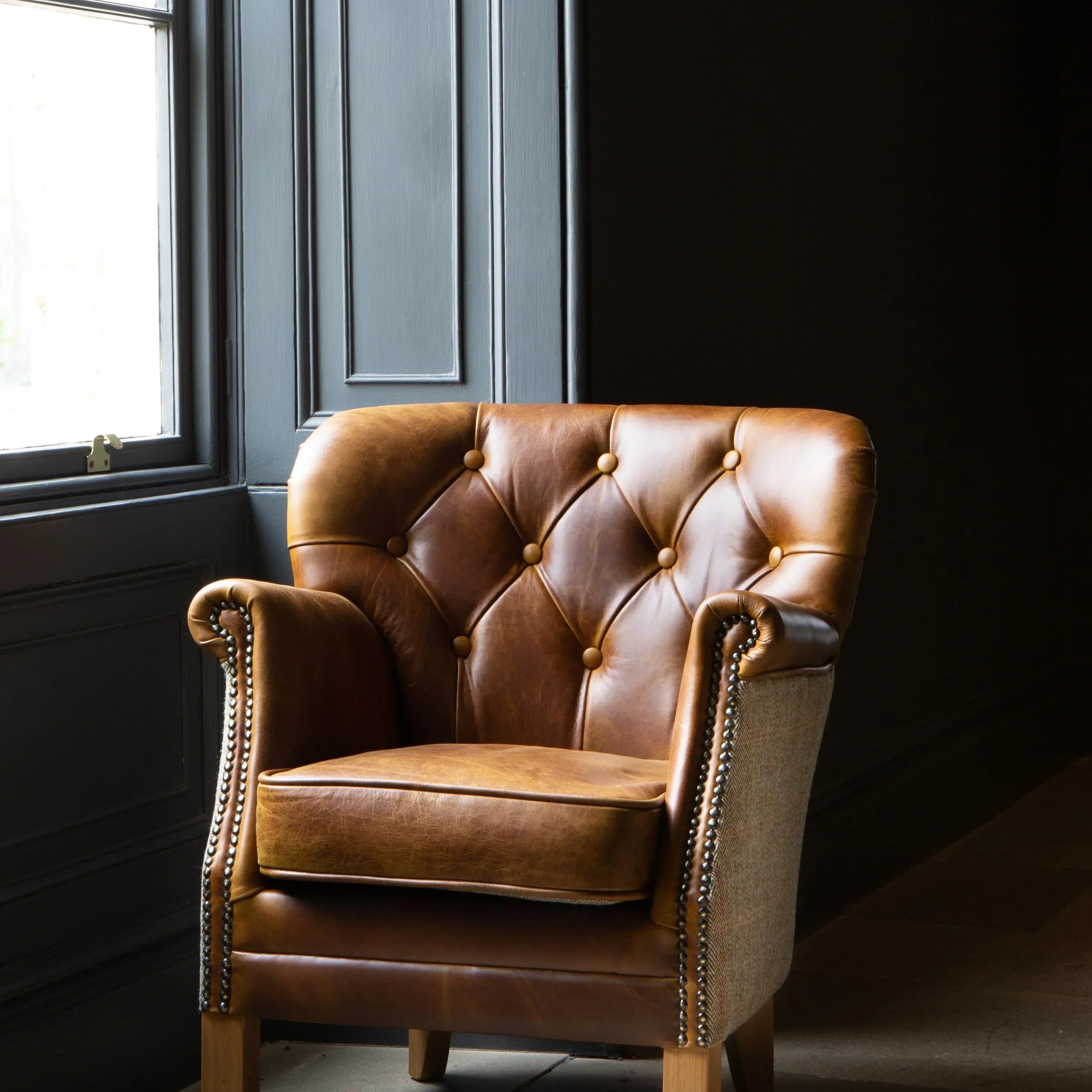 Brown leather armchair with button-tufted back and studded arms in natural light