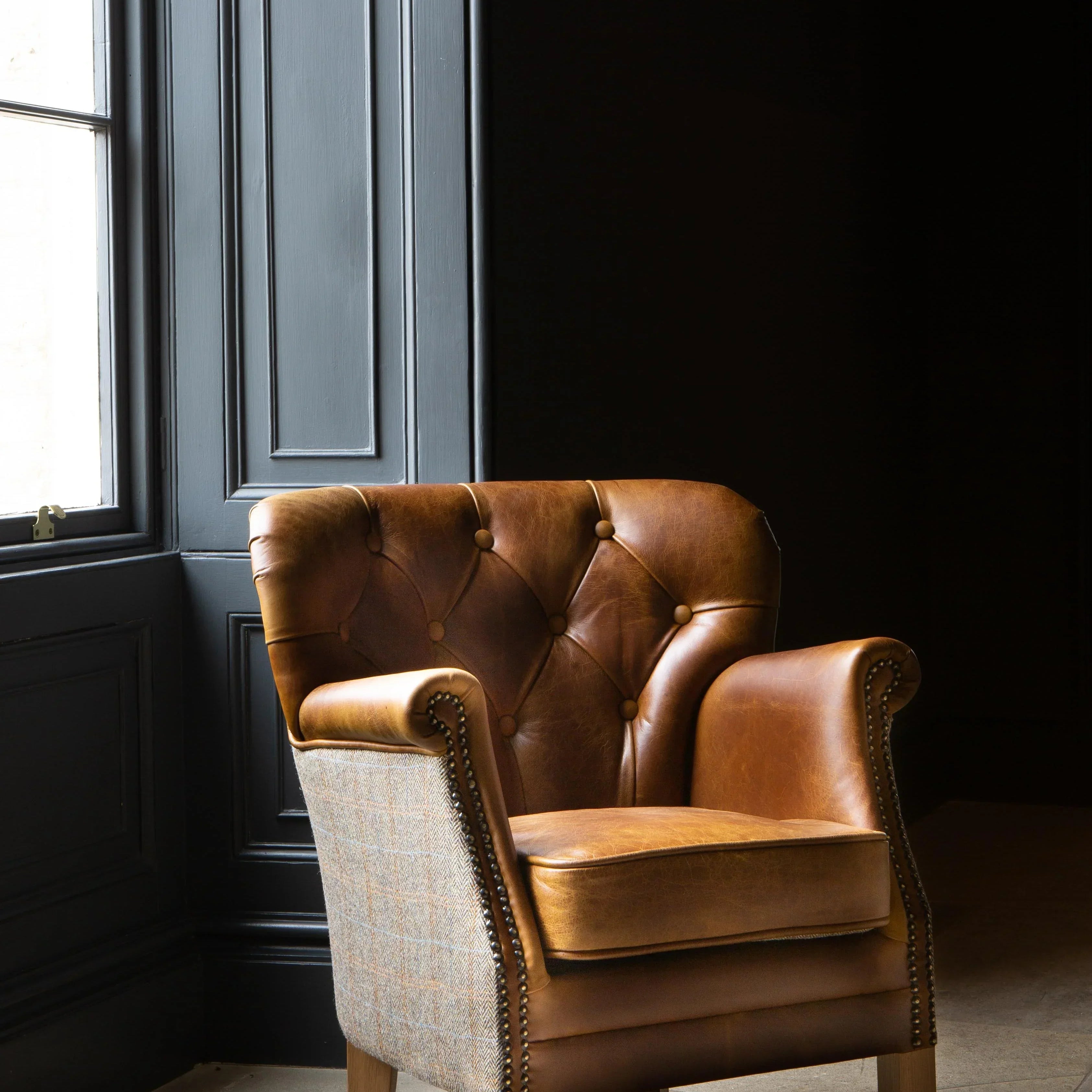 Brown leather armchair with button-tufted backrest and wooden legs near a window