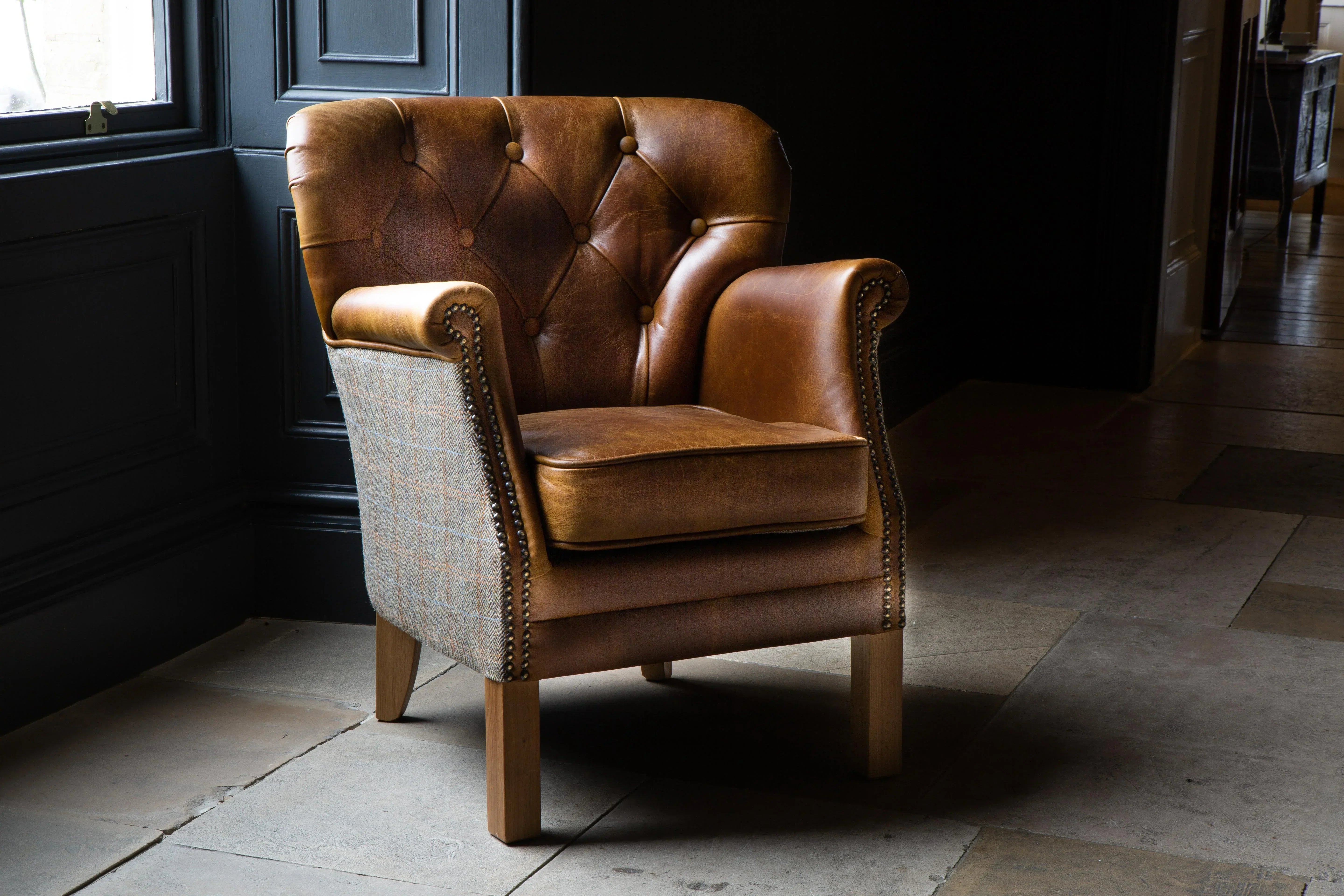Brown leather armchair with tufted back and plaid fabric sides on wooden legs