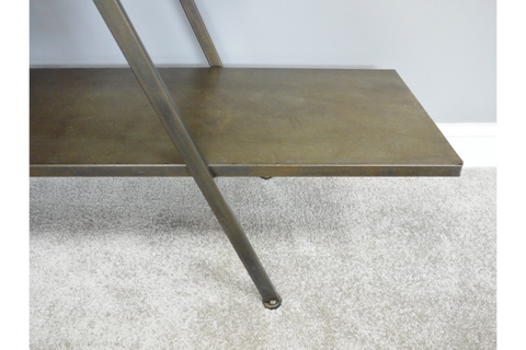 Metal display shelf in bronze finish with angled support leg on a light carpeted floor against a pale wall