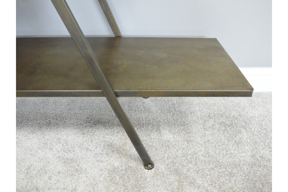 Metal display shelf in bronze finish with angled support leg on a light carpeted floor against a pale wall