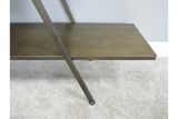 Metal display shelf in bronze finish with angled support leg on a light carpeted floor against a pale wall