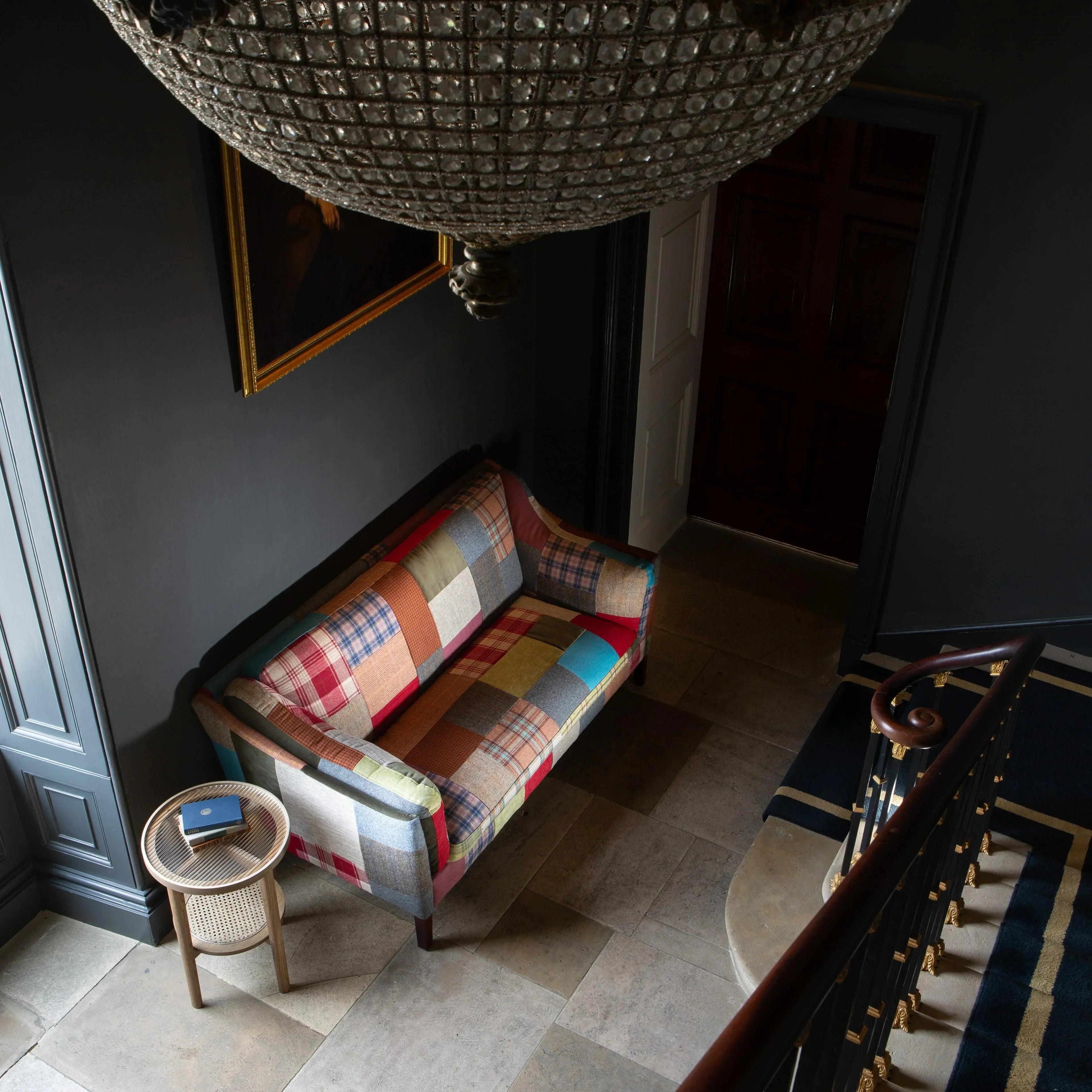 Patchwork fabric sofa with wooden legs in hallway, next to round cane side table and stairs