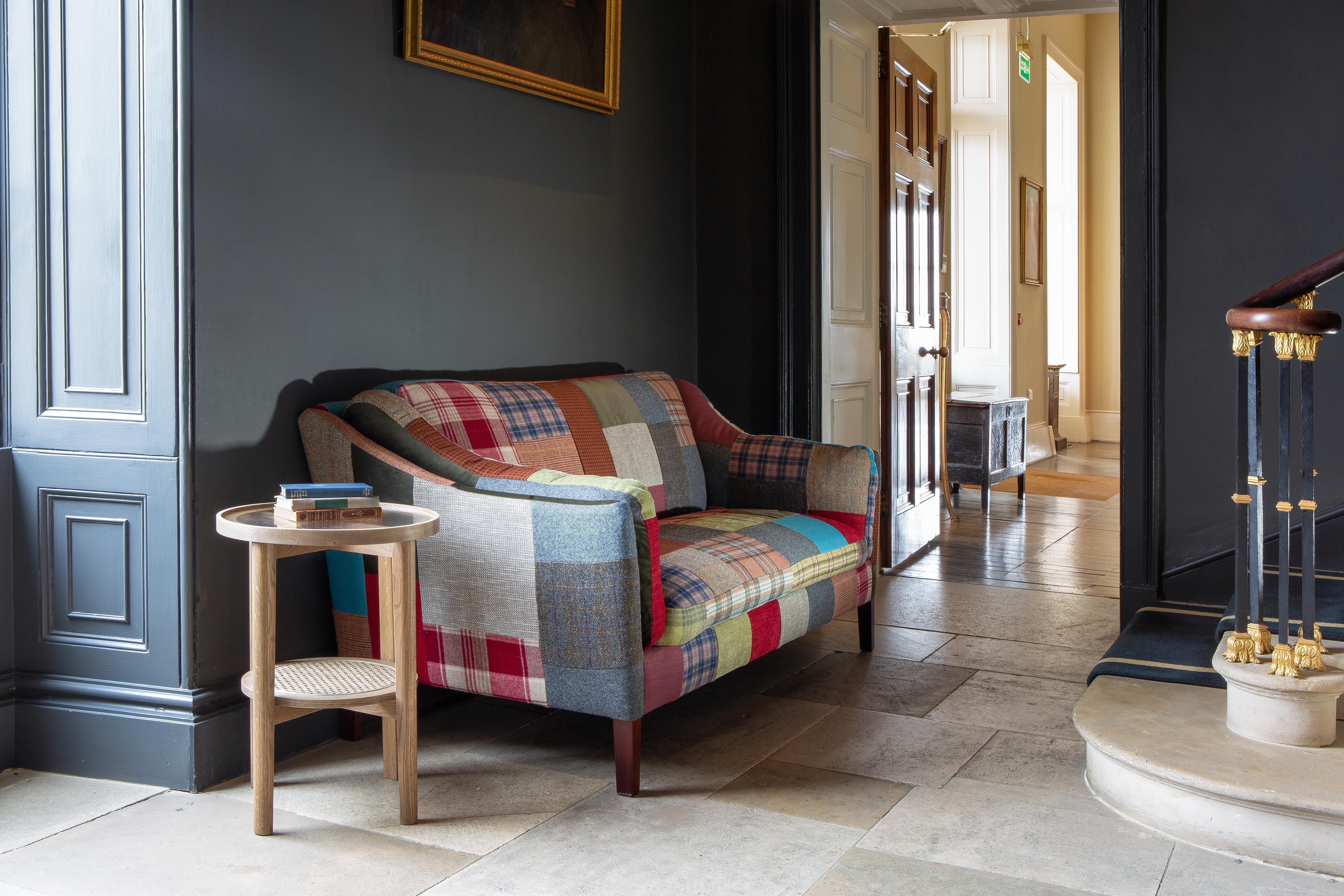 Patchwork fabric sofa with wooden legs beside round oak side table in hallway