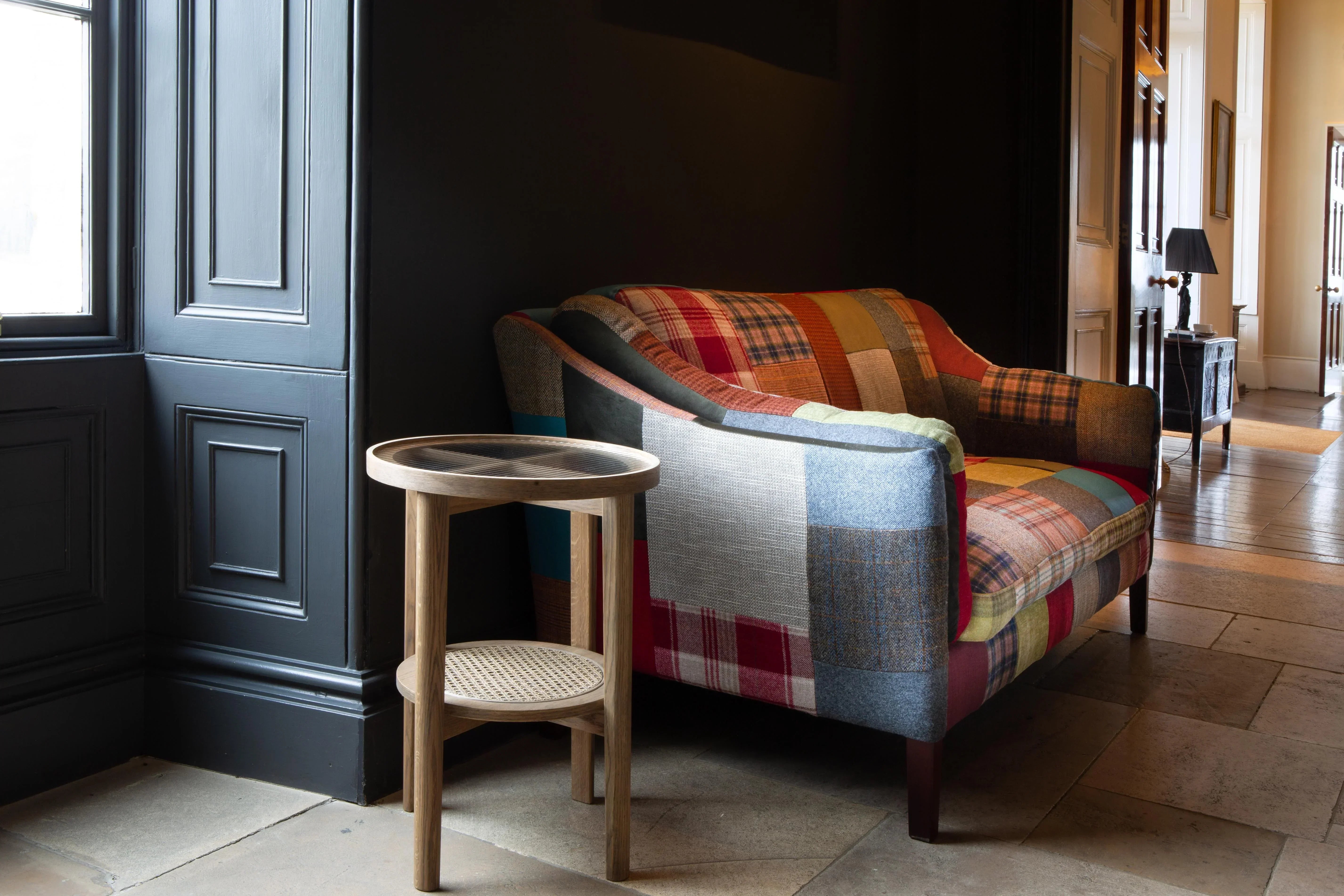 Patchwork fabric sofa and round wooden side table in a hallway with tiled floor