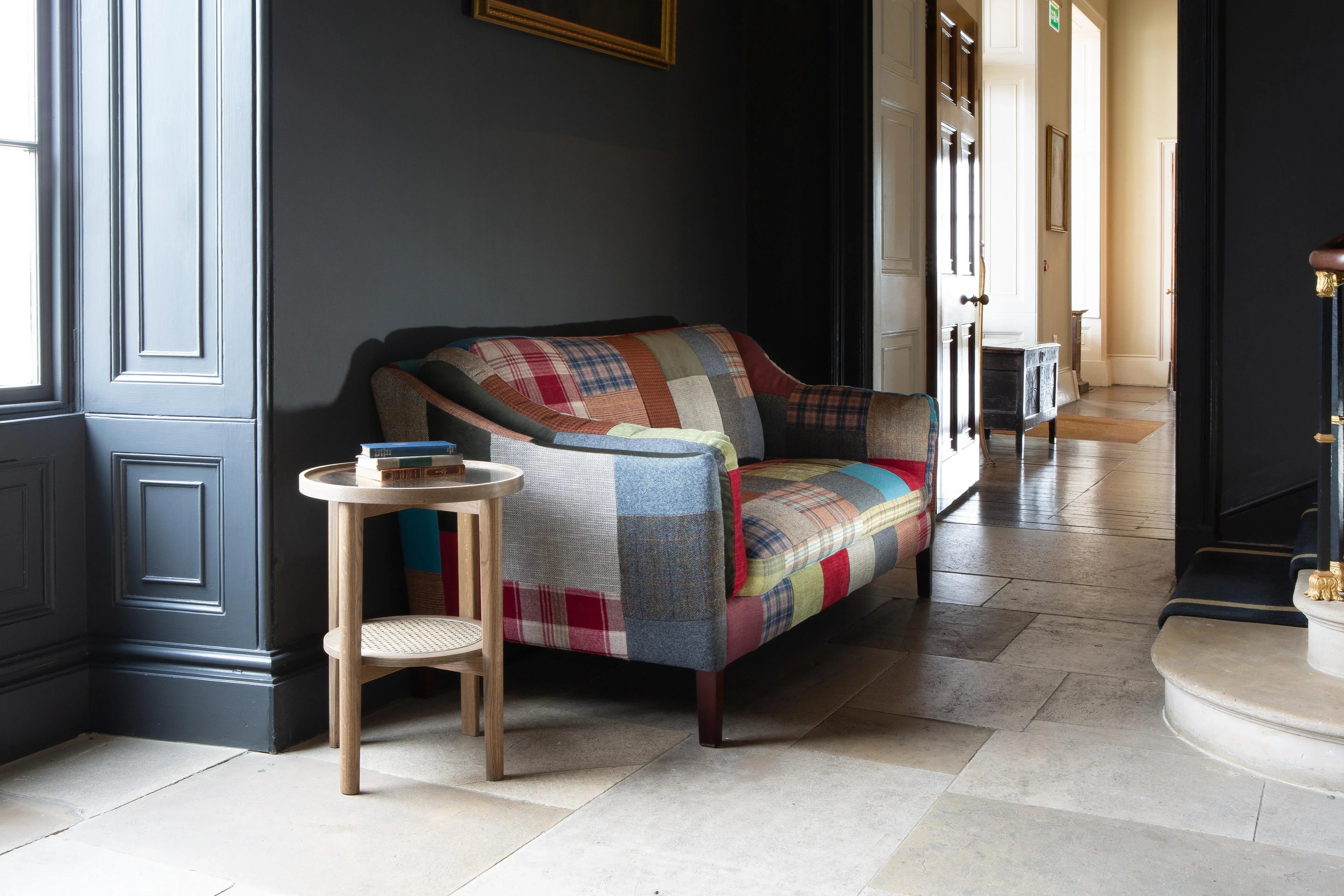 Patchwork fabric sofa with wooden legs in hallway, round side table with books beside