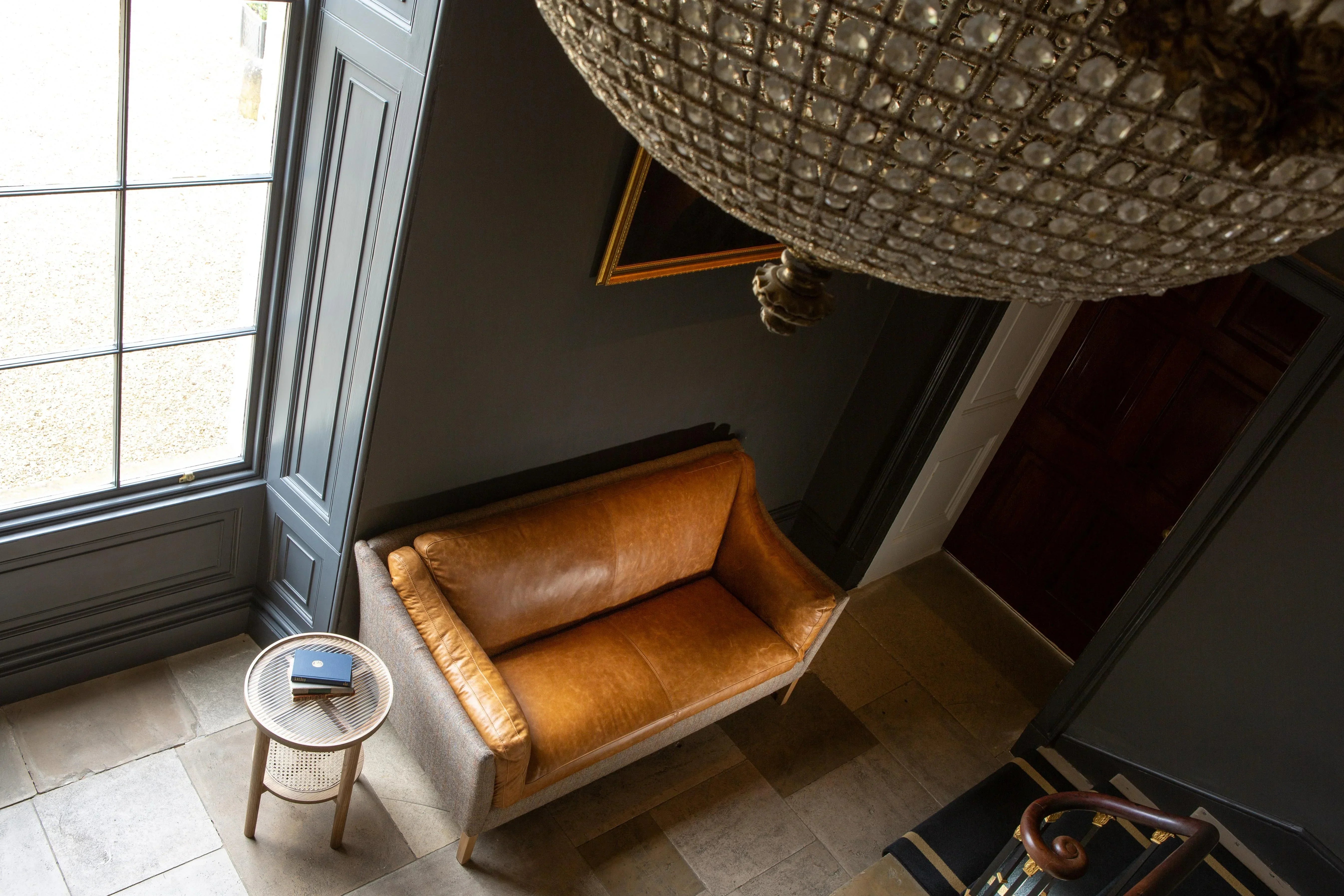 Tan leather sofa with wooden legs beside round side table in hallway near large window