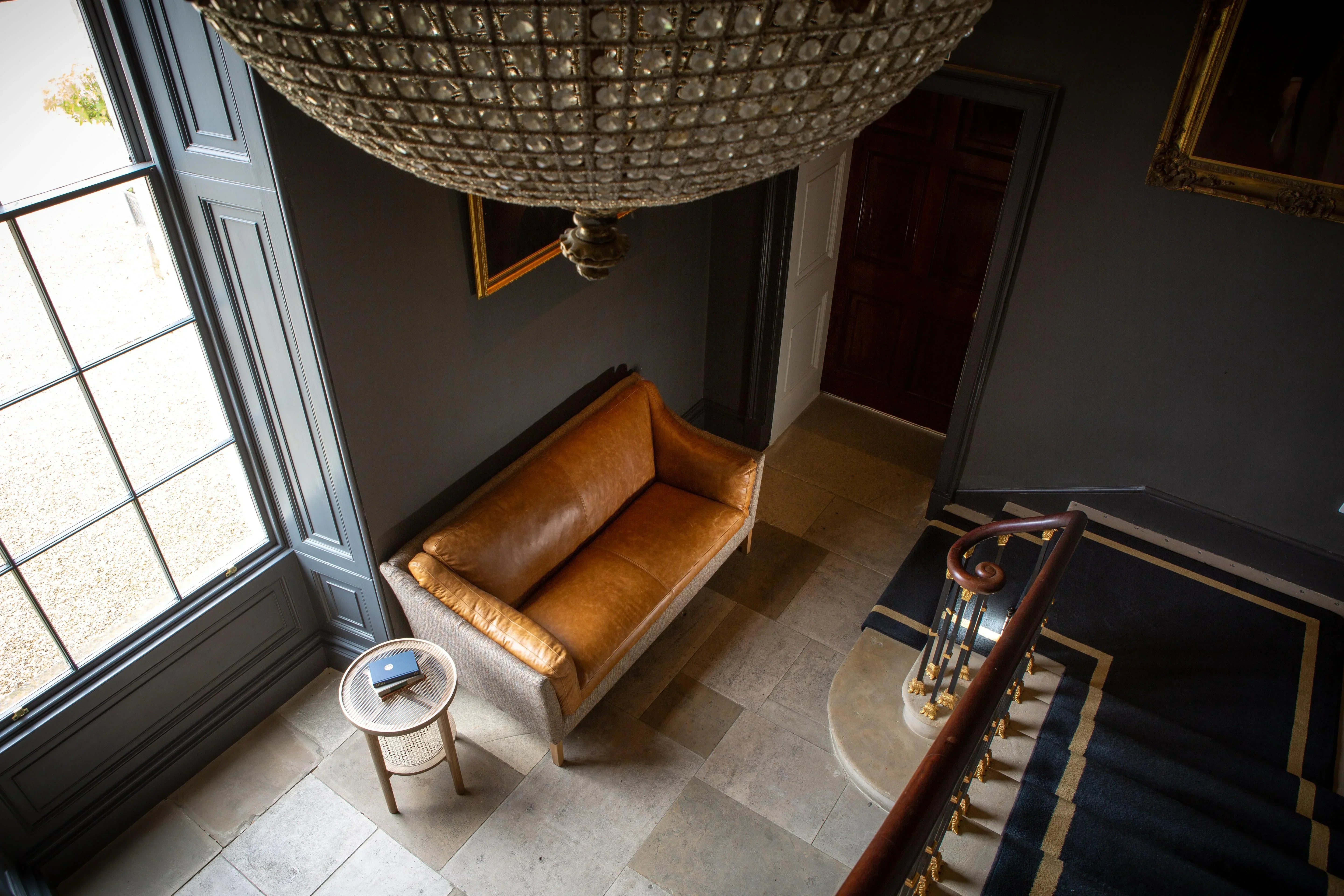 Tan leather sofa with wooden legs in hallway next to side table and large window