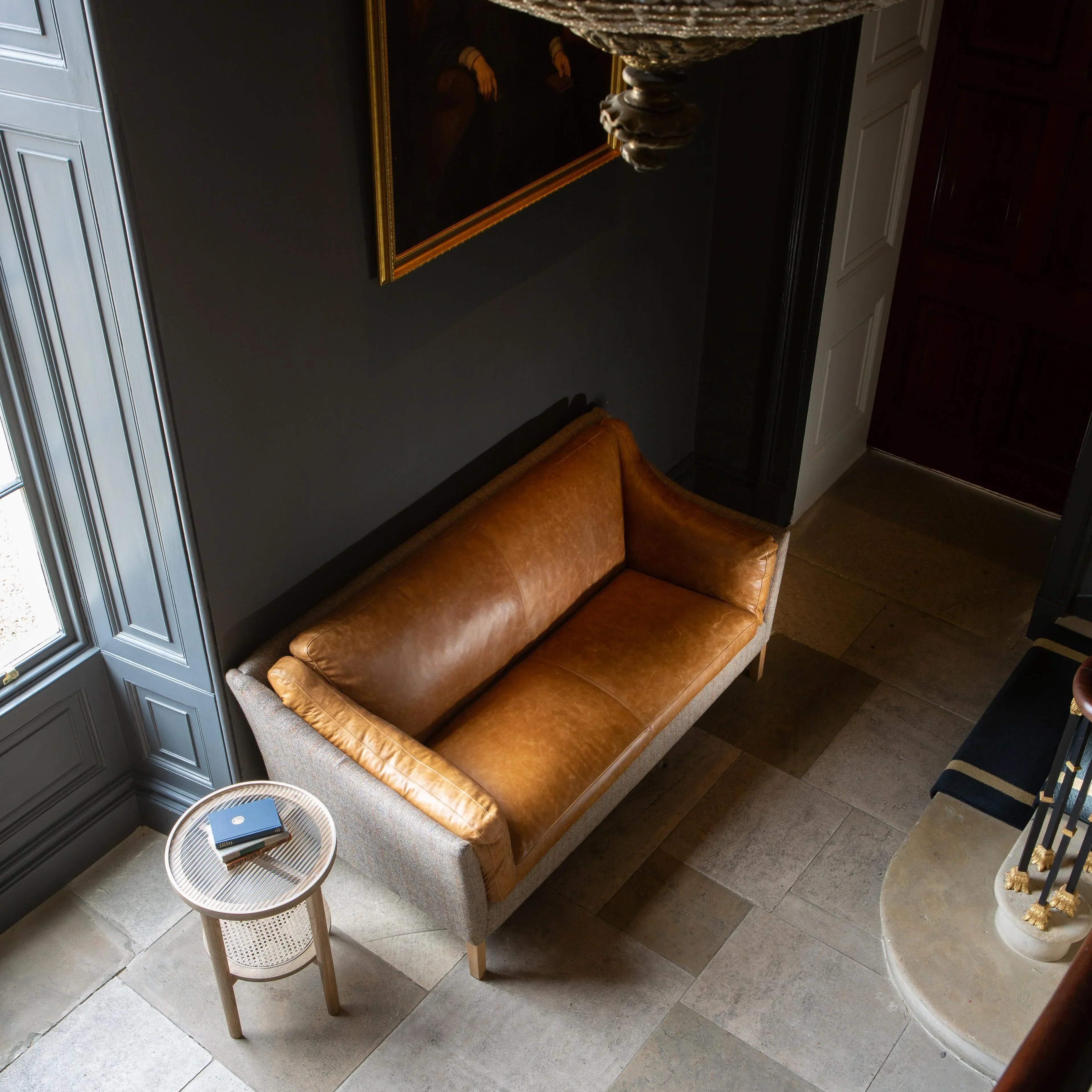 Tan leather sofa with fabric sides in hallway beside small round side table