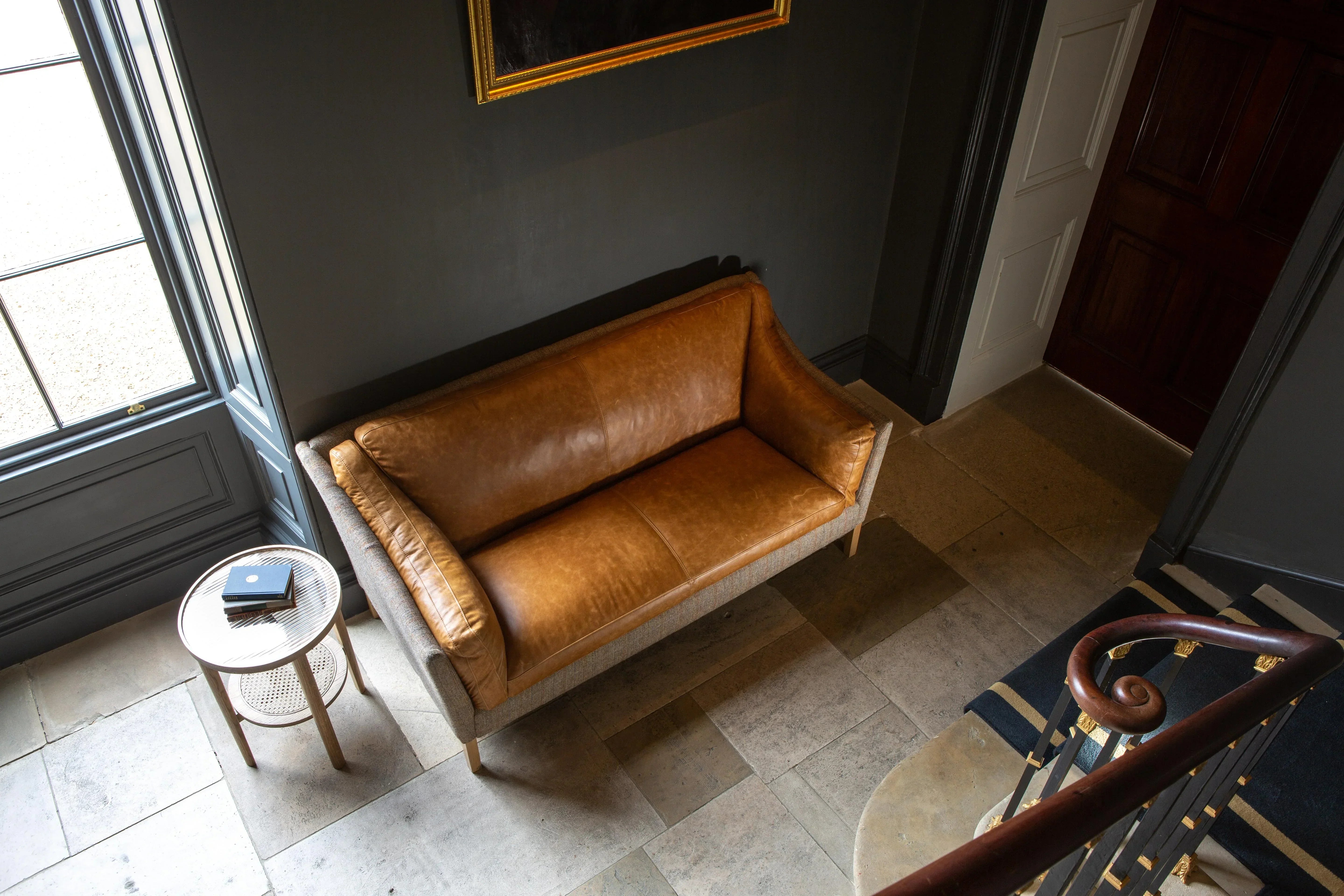 Tan leather sofa with wooden legs and side table in hallway with tiled floor