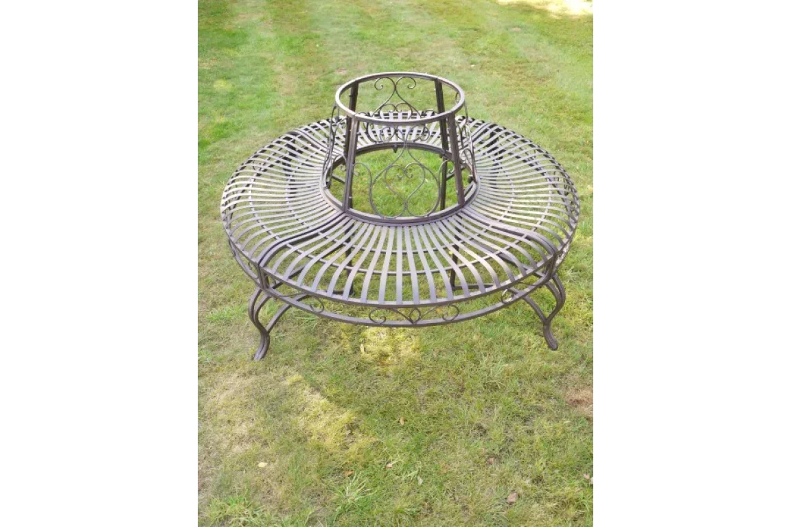 Circular metal garden bench with decorative scrollwork on grass