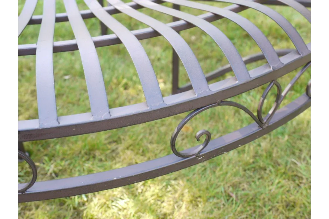 Closeup of metal garden bench with curved slats and decorative scrollwork on grassy lawn