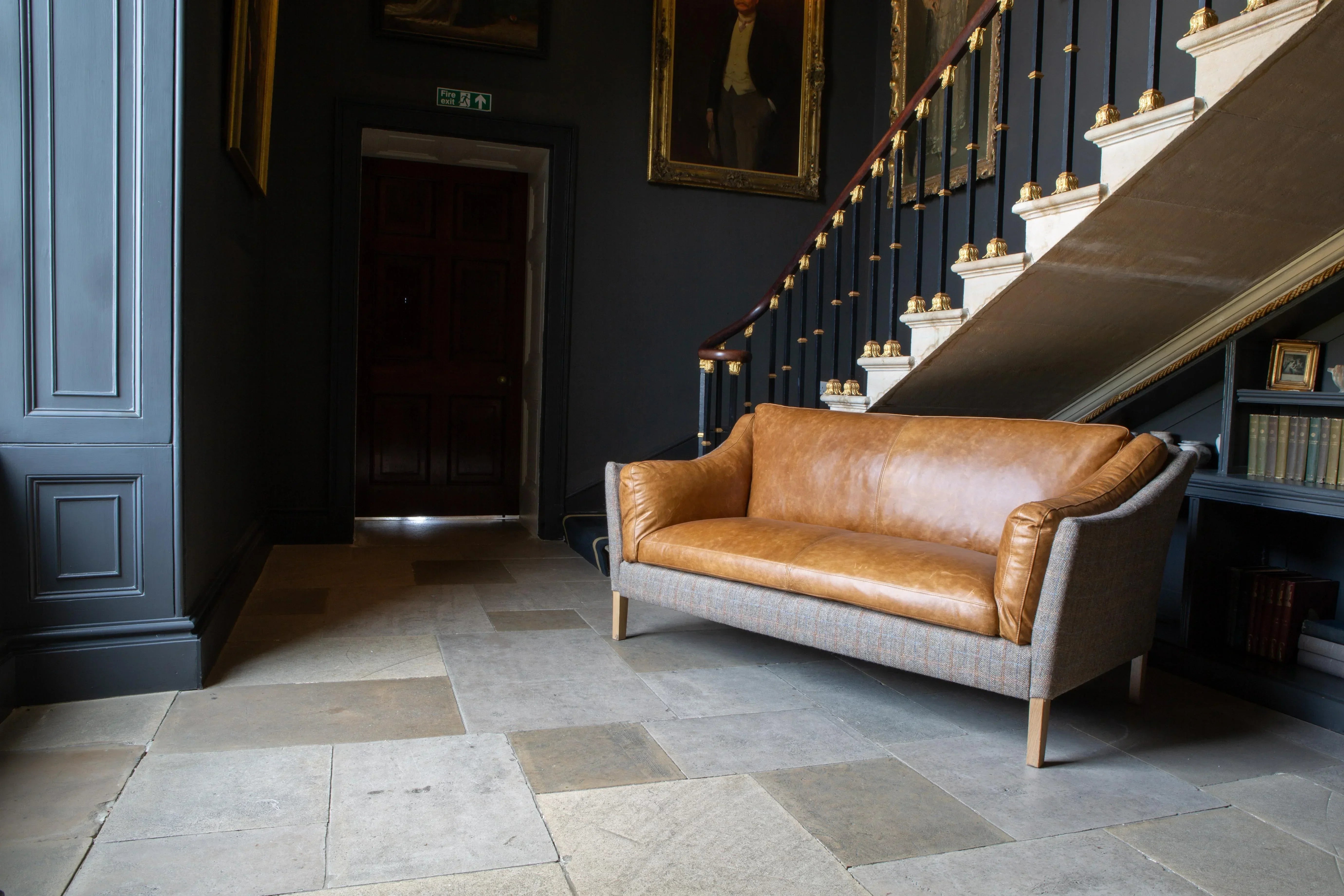 Brown leather sofa with fabric sides in a hallway by a staircase and classic portraits