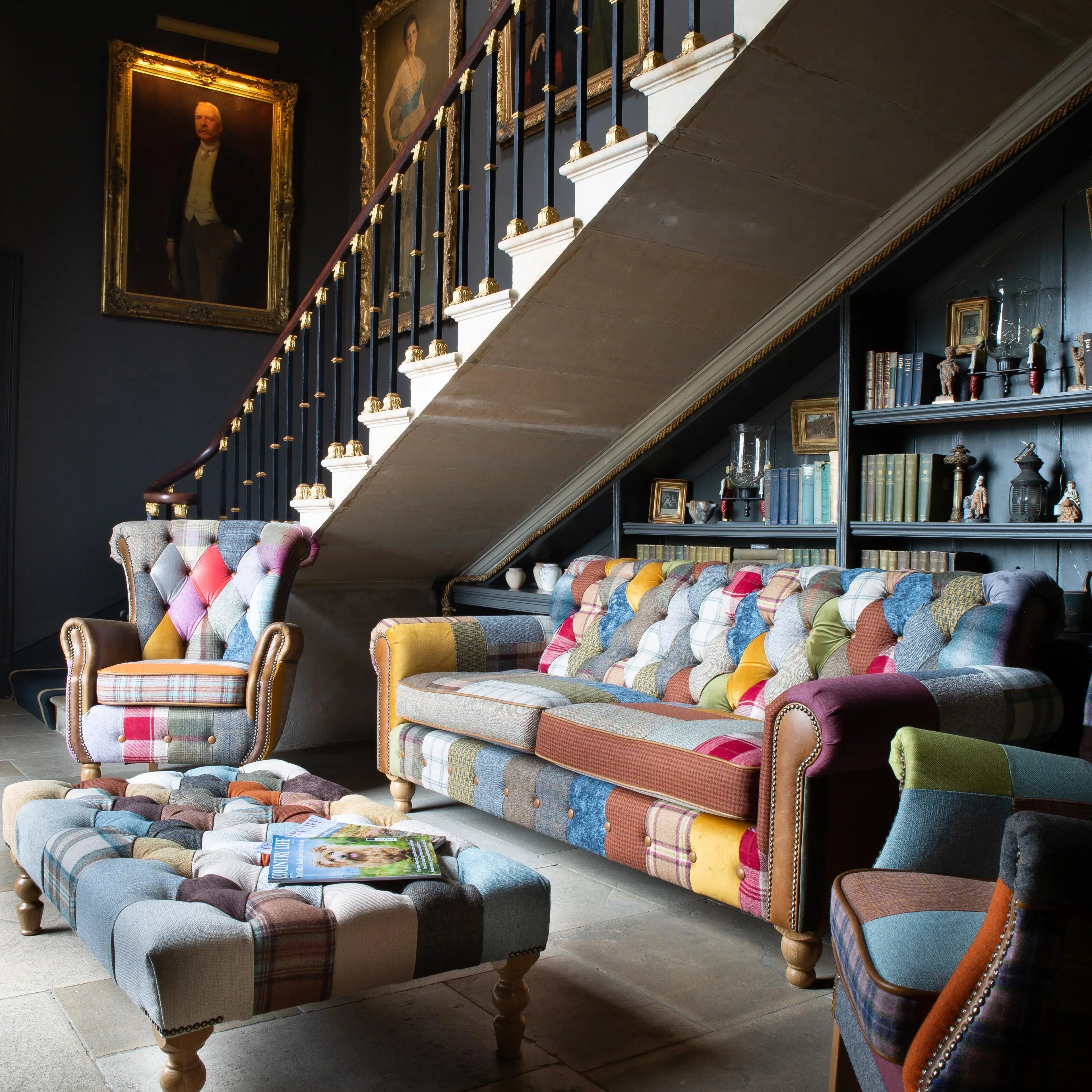 Patchwork armchair, sofa, and footstool set in traditional lounge with staircase and portraits