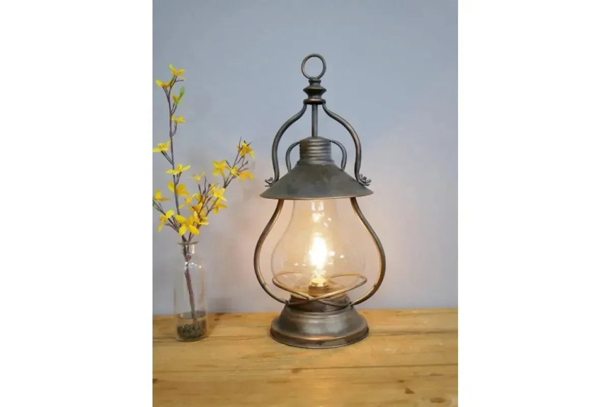 Vintage lantern table lamp with glass shade on wooden surface beside yellow artificial flowers