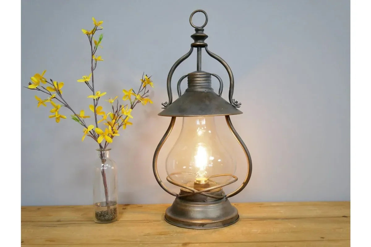 Rustic metal table lamp with exposed bulb beside clear vase of yellow artificial flowers