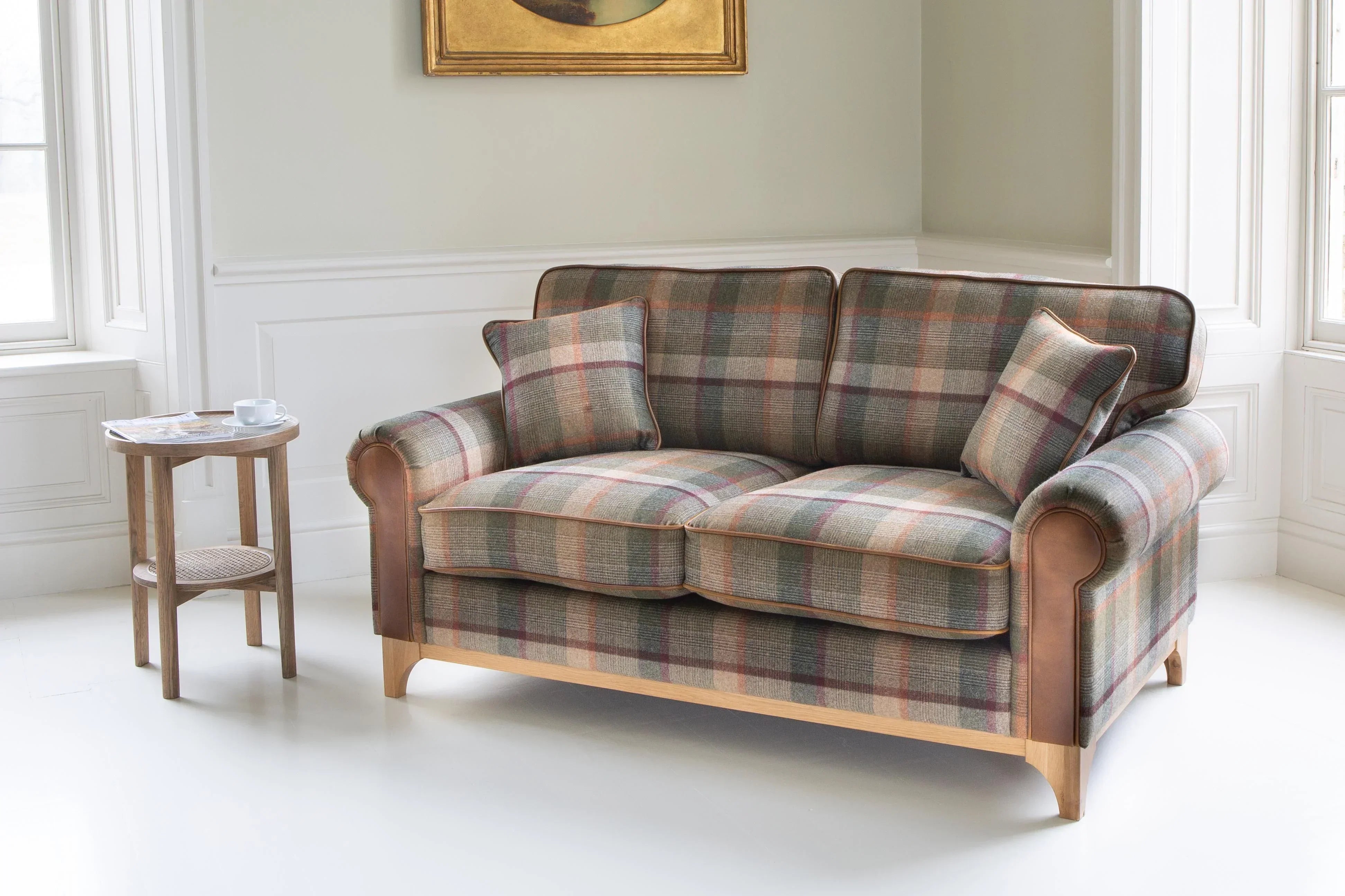 Tartan fabric two seater sofa with wooden base in bright living room, matching scatter cushions