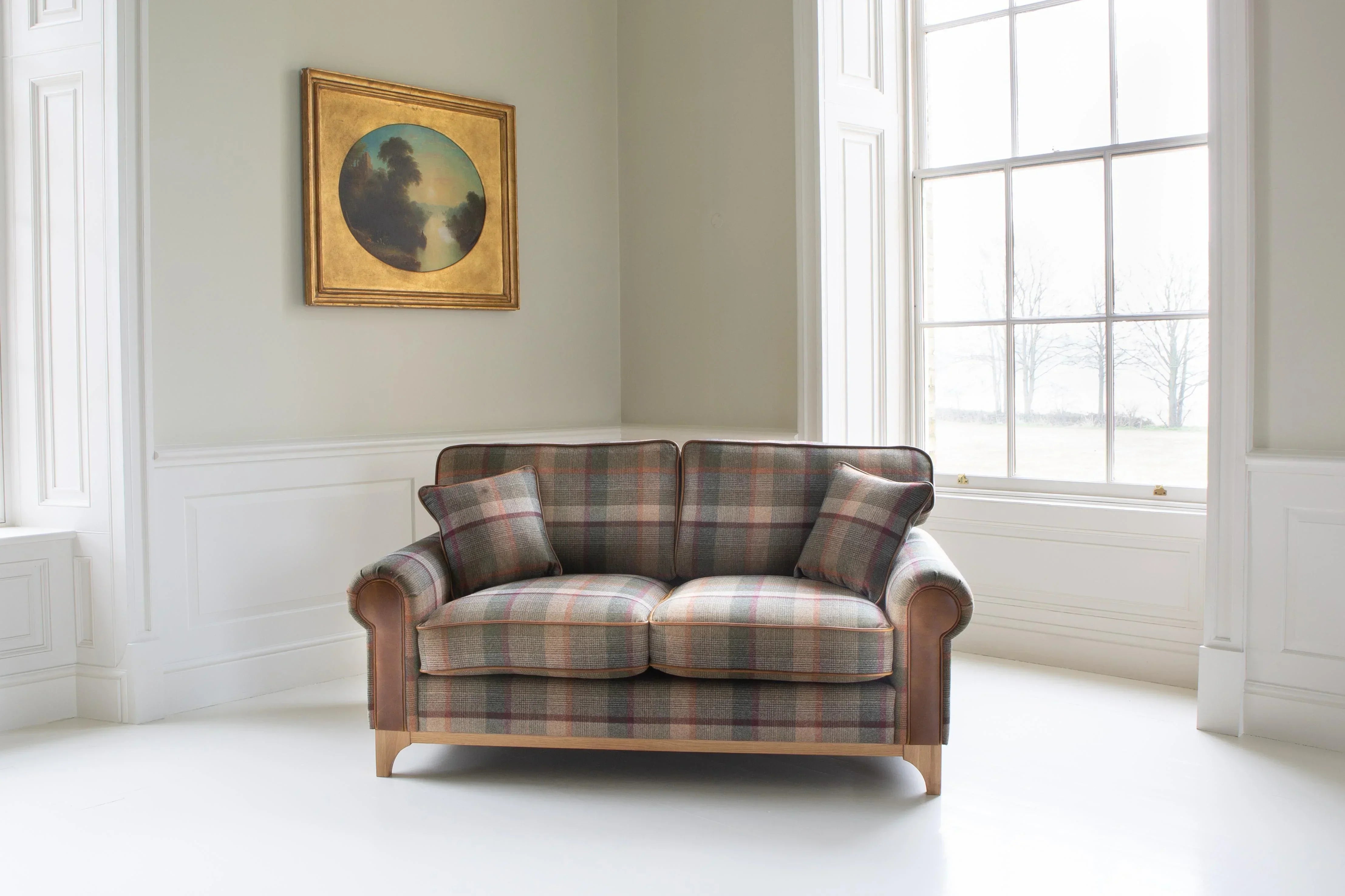 Plaid fabric two-seater sofa with wooden legs in bright living room, includes matching cushions