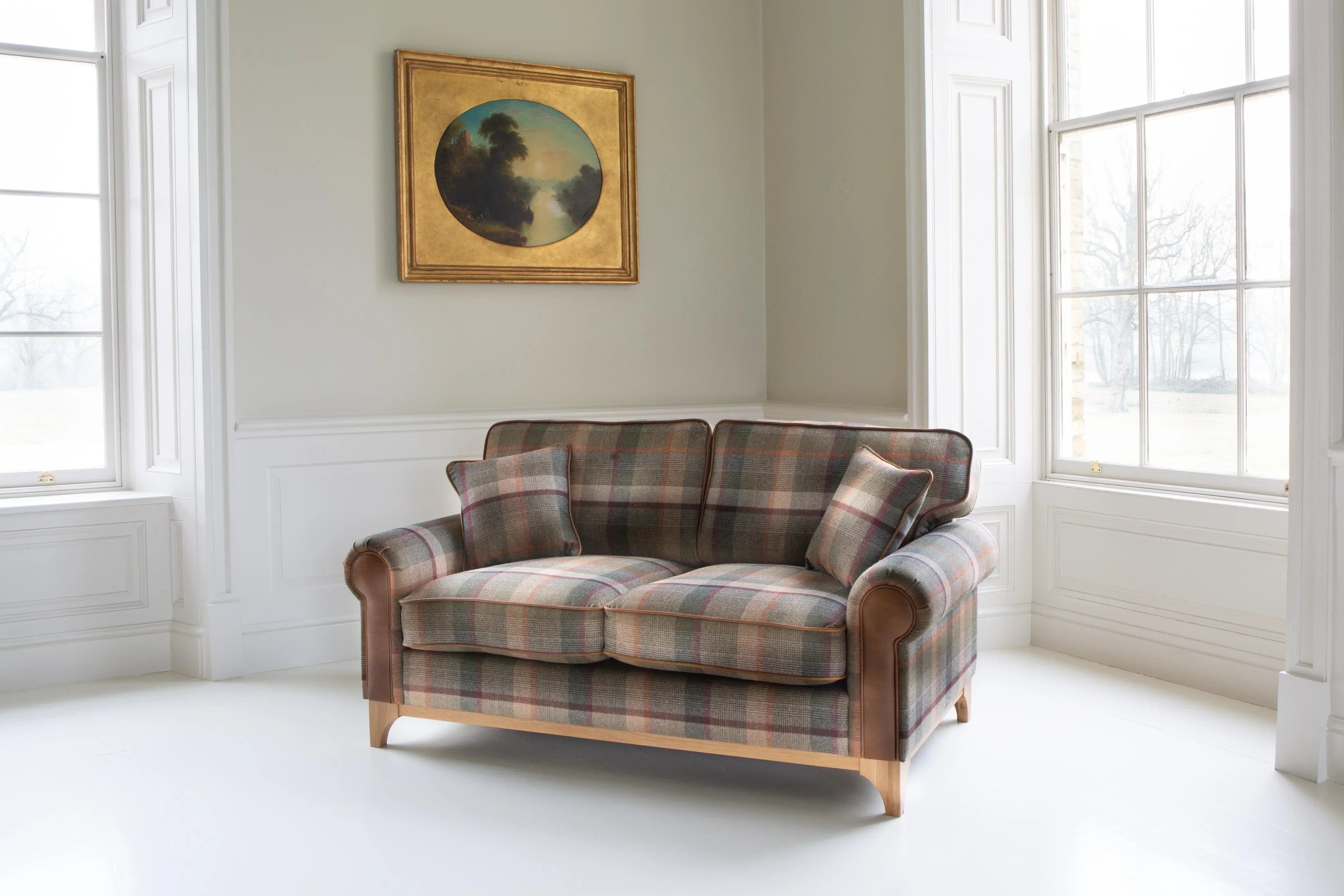 Plaid fabric two-seater sofa with leather arms and wooden legs in a bright living room