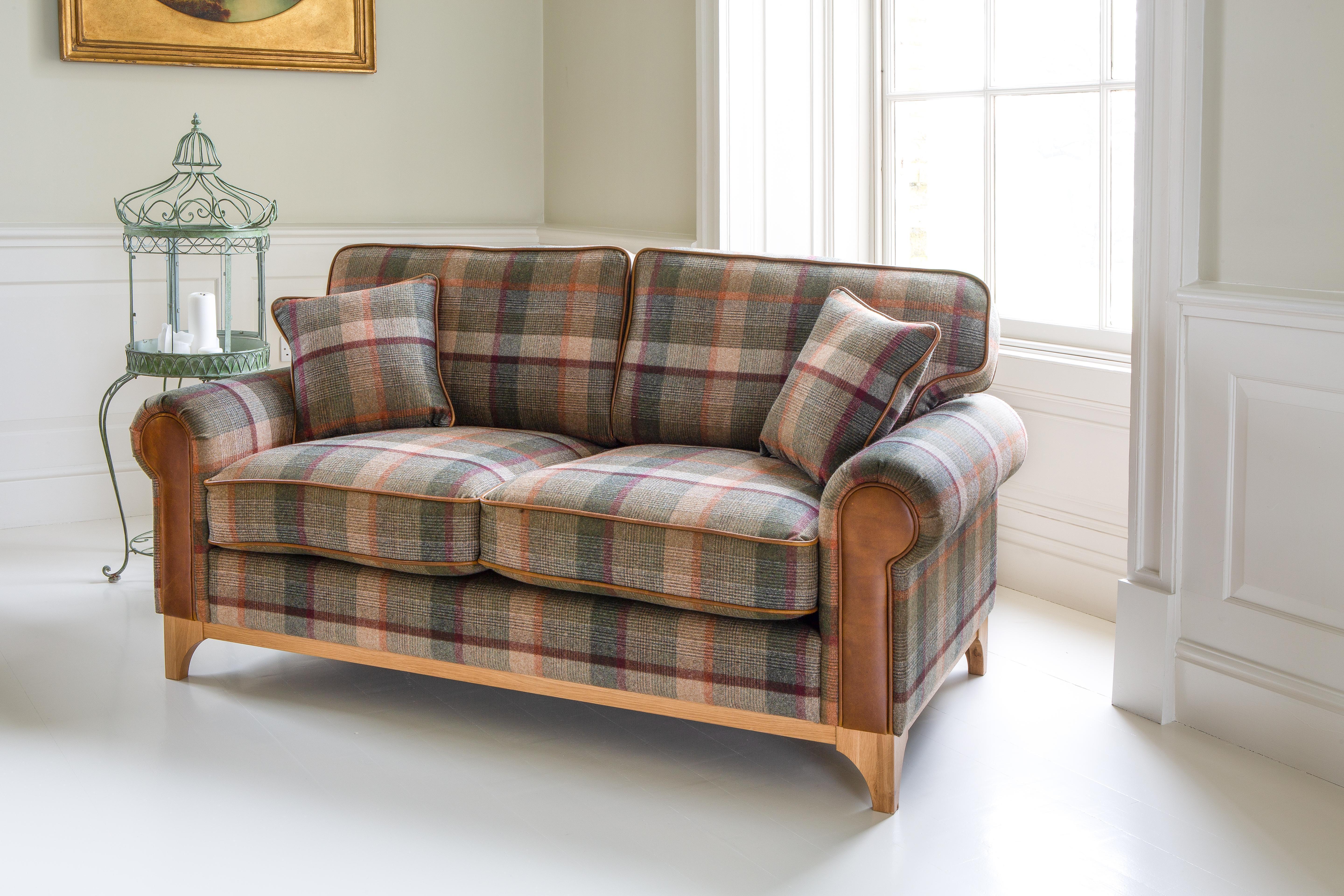 Plaid fabric two-seater sofa with wooden legs and brown armrests in a bright living room