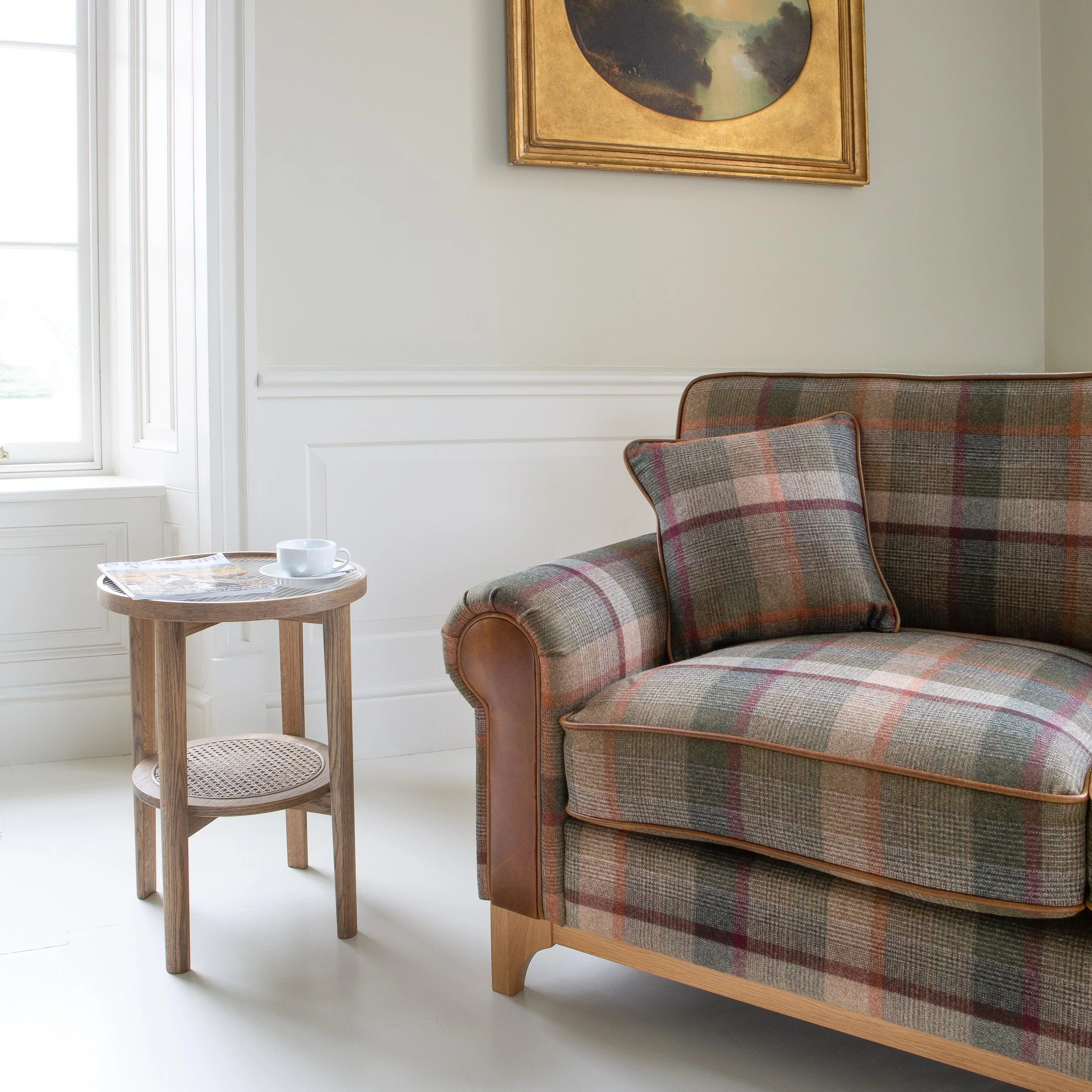 Plaid fabric sofa with leather arms beside wooden side table and framed wall art in living room
