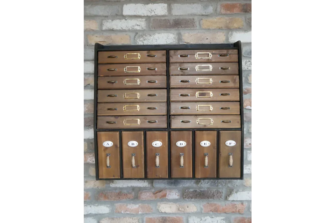Vintage wooden cabinet with multiple labeled drawers mounted on brick wall