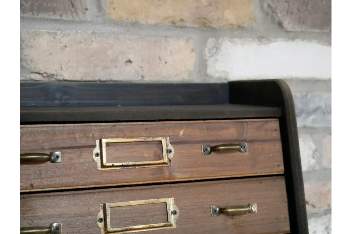 Wooden drawer unit with brass handles and label holders against brick wall