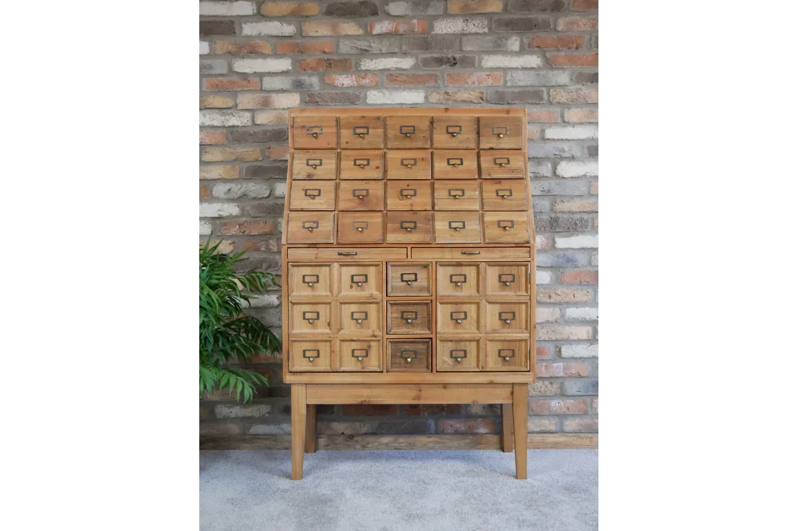 Wooden storage cabinet with multiple drawers and label holders against brick wall
