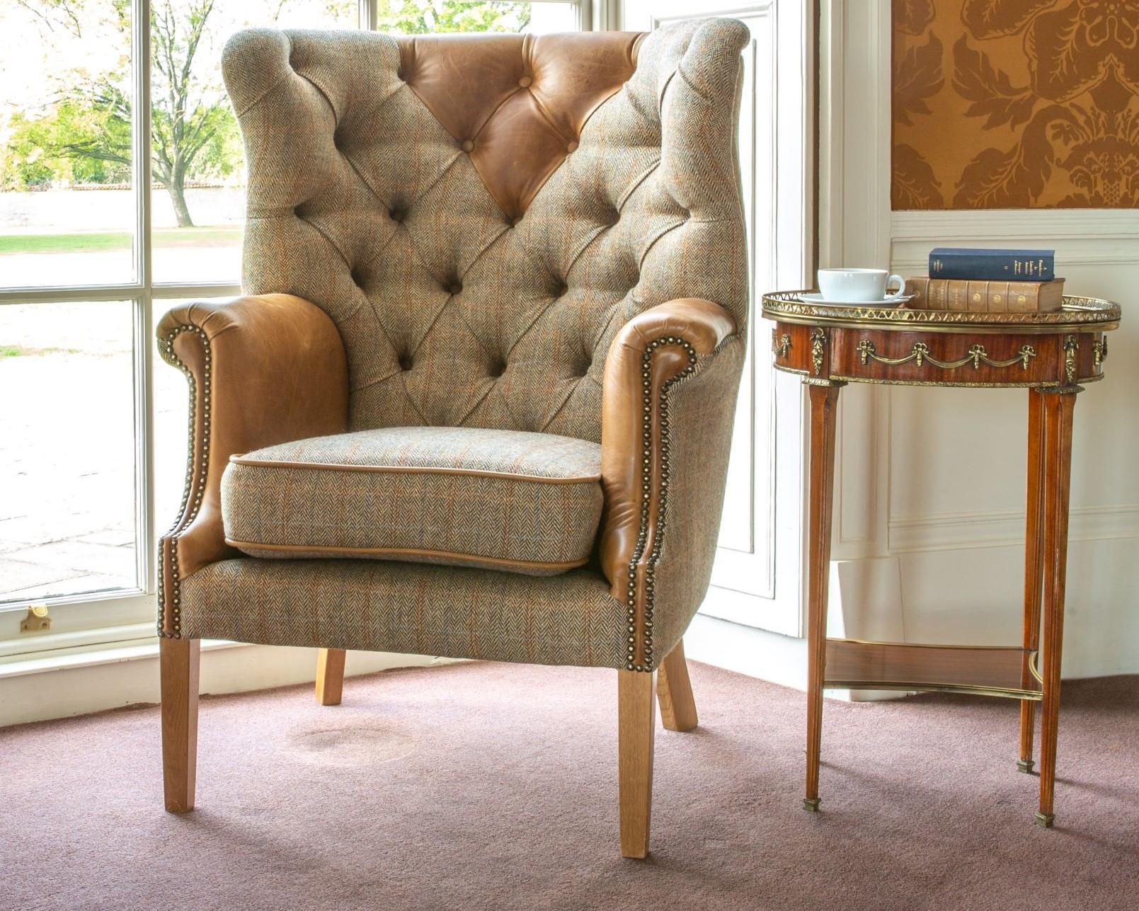 Wingback accent chair with tufted fabric and tan leather arms beside a wooden side table