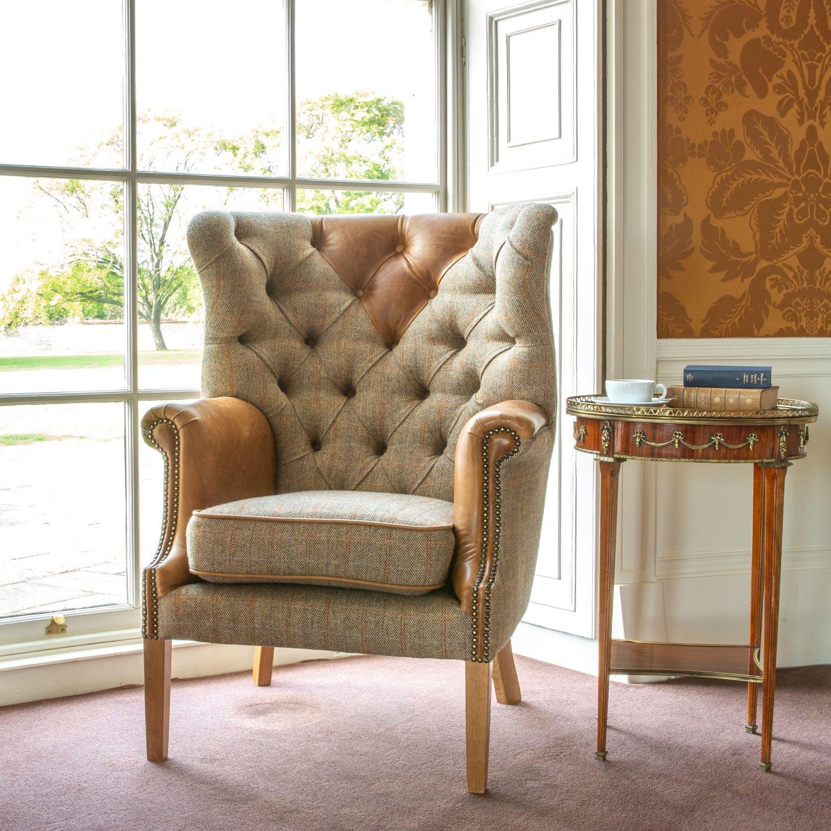 Button-tufted armchair with tweed fabric and tan leather accents beside window and side table