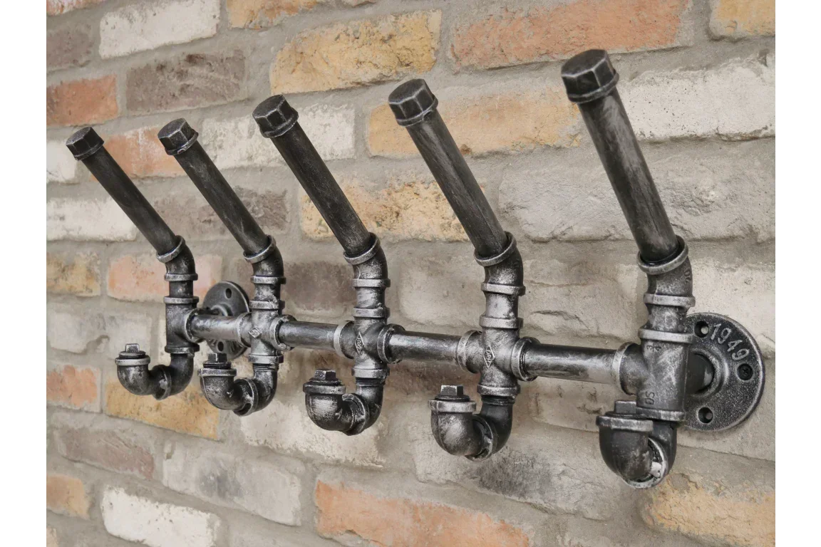 Industrial style metal coat rack with five pipe hooks mounted on brick wall