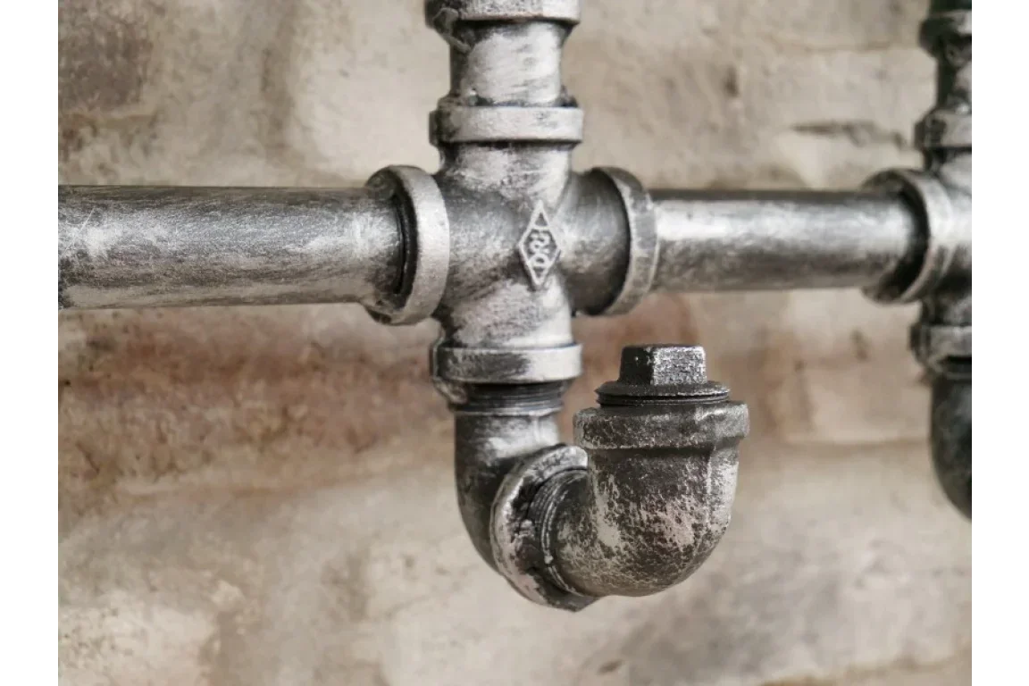 Close-up of industrial metal pipe fitting with vintage finish against brick wall