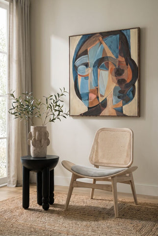 Grey fabric chair featuring a cane backrest and washed elm wood frame, positioned beside a round black side table with a textured surface.