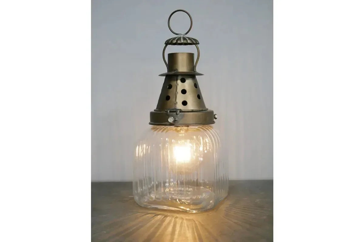 Vintage glass table lamp with ribbed base and antique brass top, lit on wooden surface