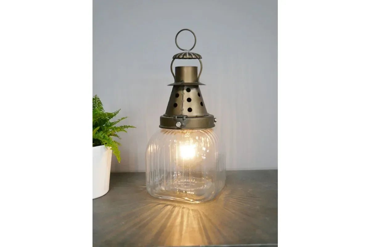 Vintage glass lantern lamp with metal top on grey surface beside potted plant