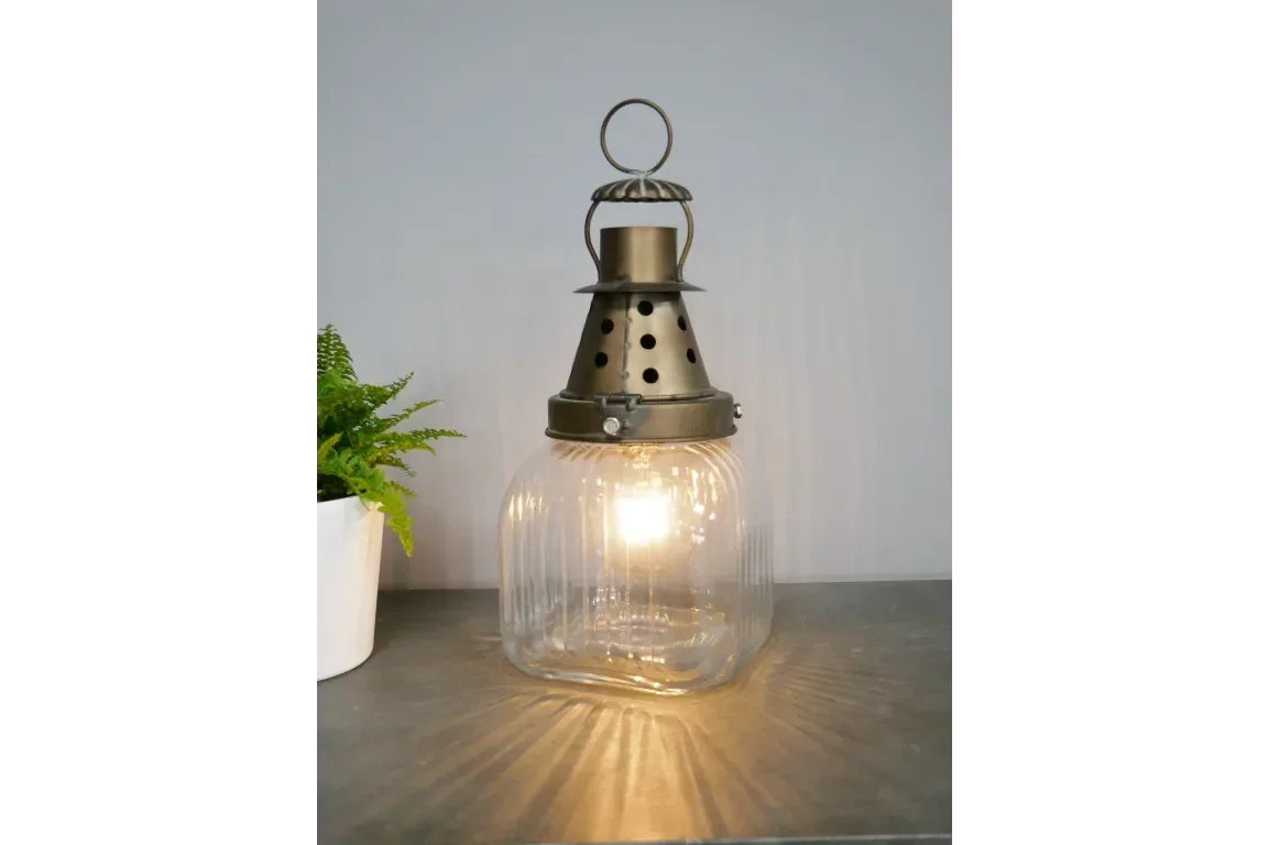 Vintage glass lantern table lamp with brass top on grey surface next to potted plant