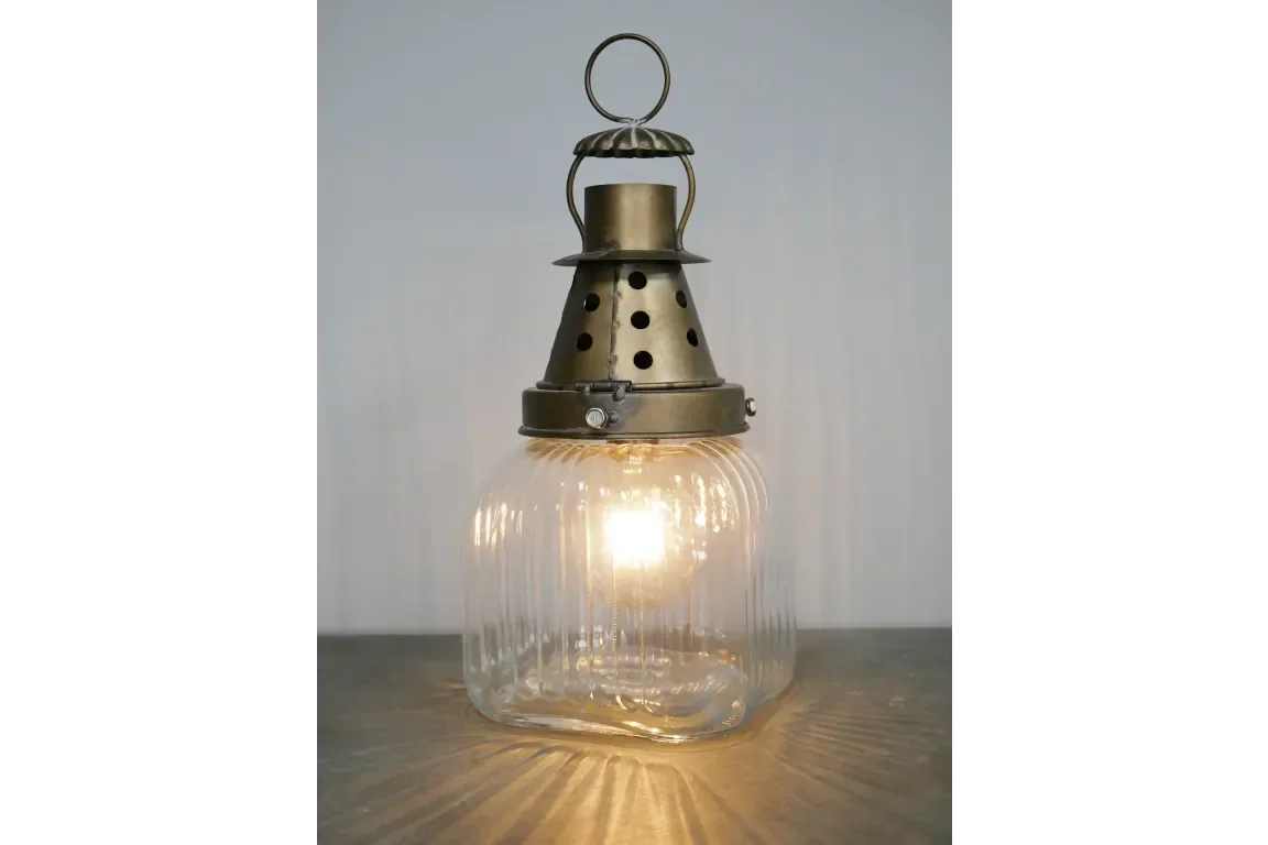 Vintage glass table lamp with ribbed shade and brass metal top, lit on wooden surface