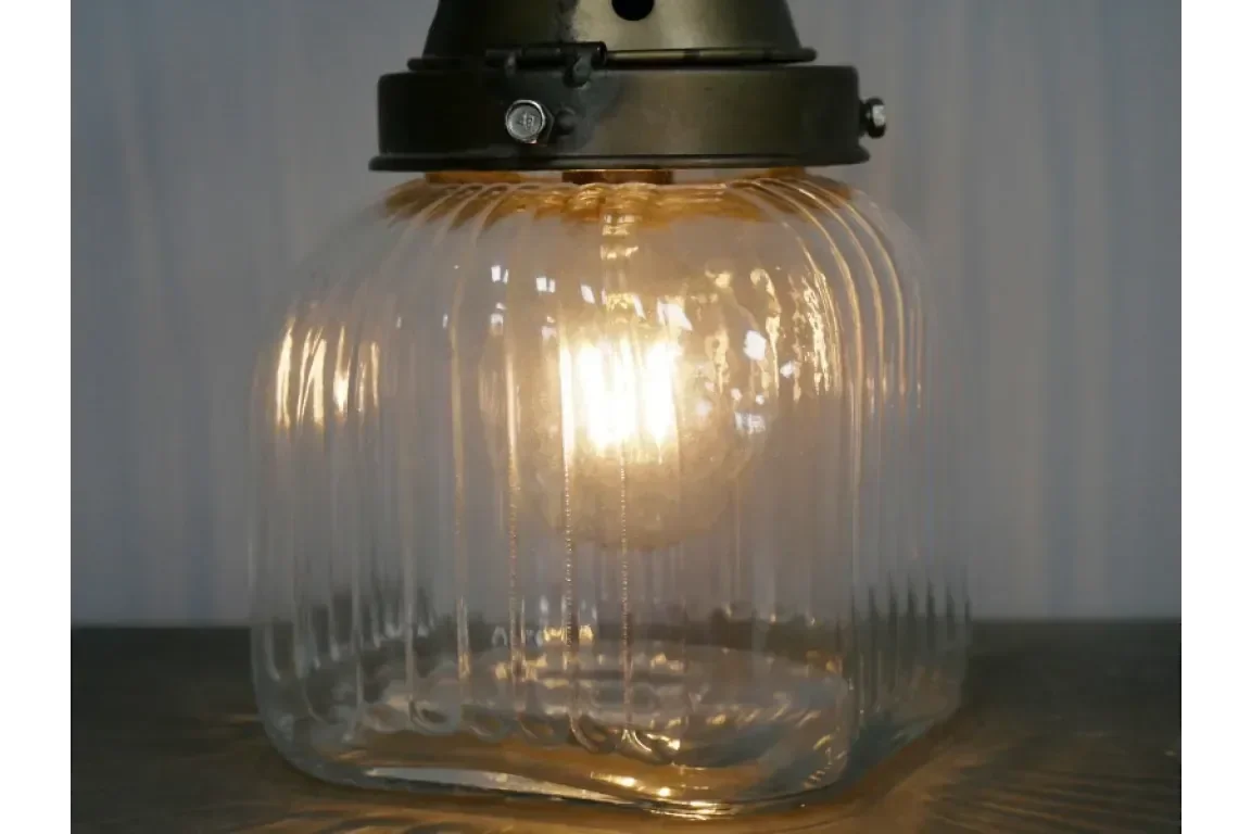 Glass pendant light with ribbed shade and exposed bulb on wooden surface