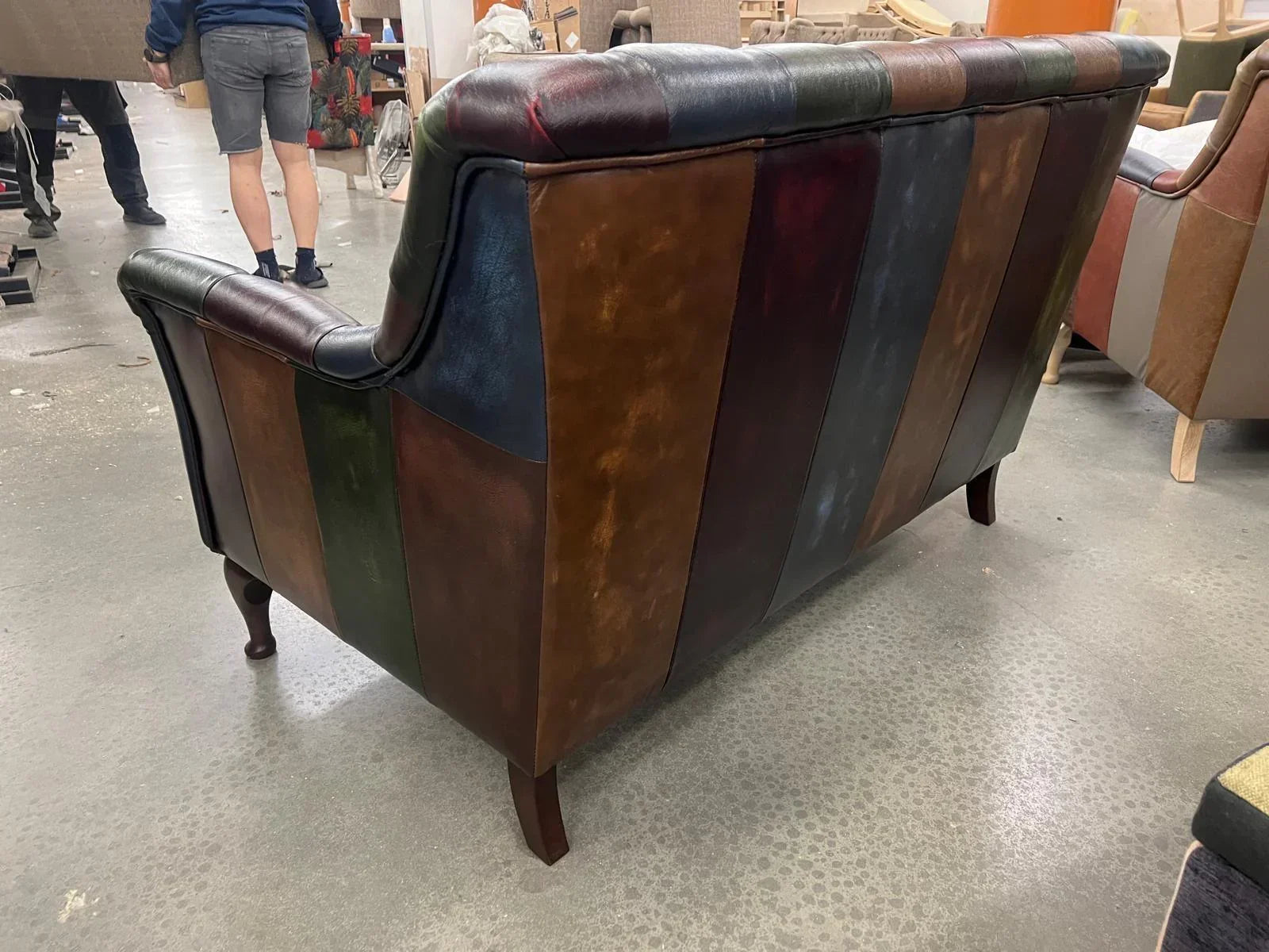Back view of patchwork leather sofa with wooden legs in workshop setting