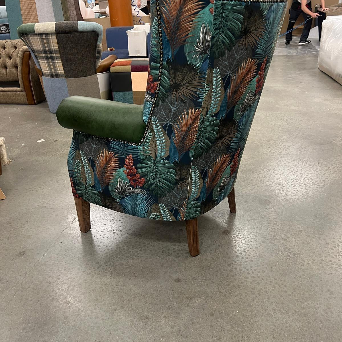 Floral wingback armchair with green velvet armrest and wooden legs on showroom floor